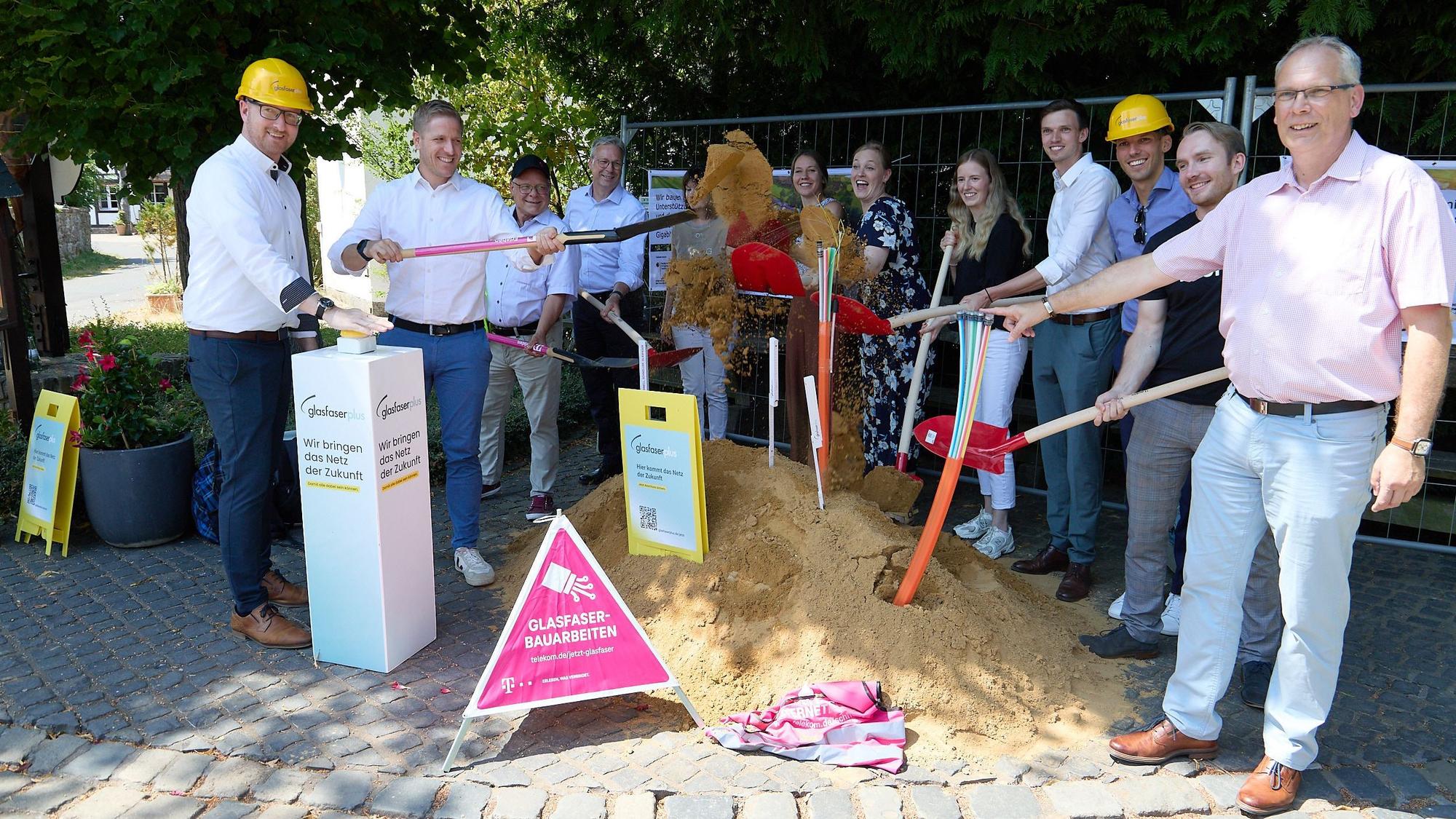Die Vertreter der Kommunen und der beteiligten Firmen haben sich im Halbkreis um einen Sandhügel gruppiert, um mit Schaufeln den ersten Spatenstich durchzuführen.
