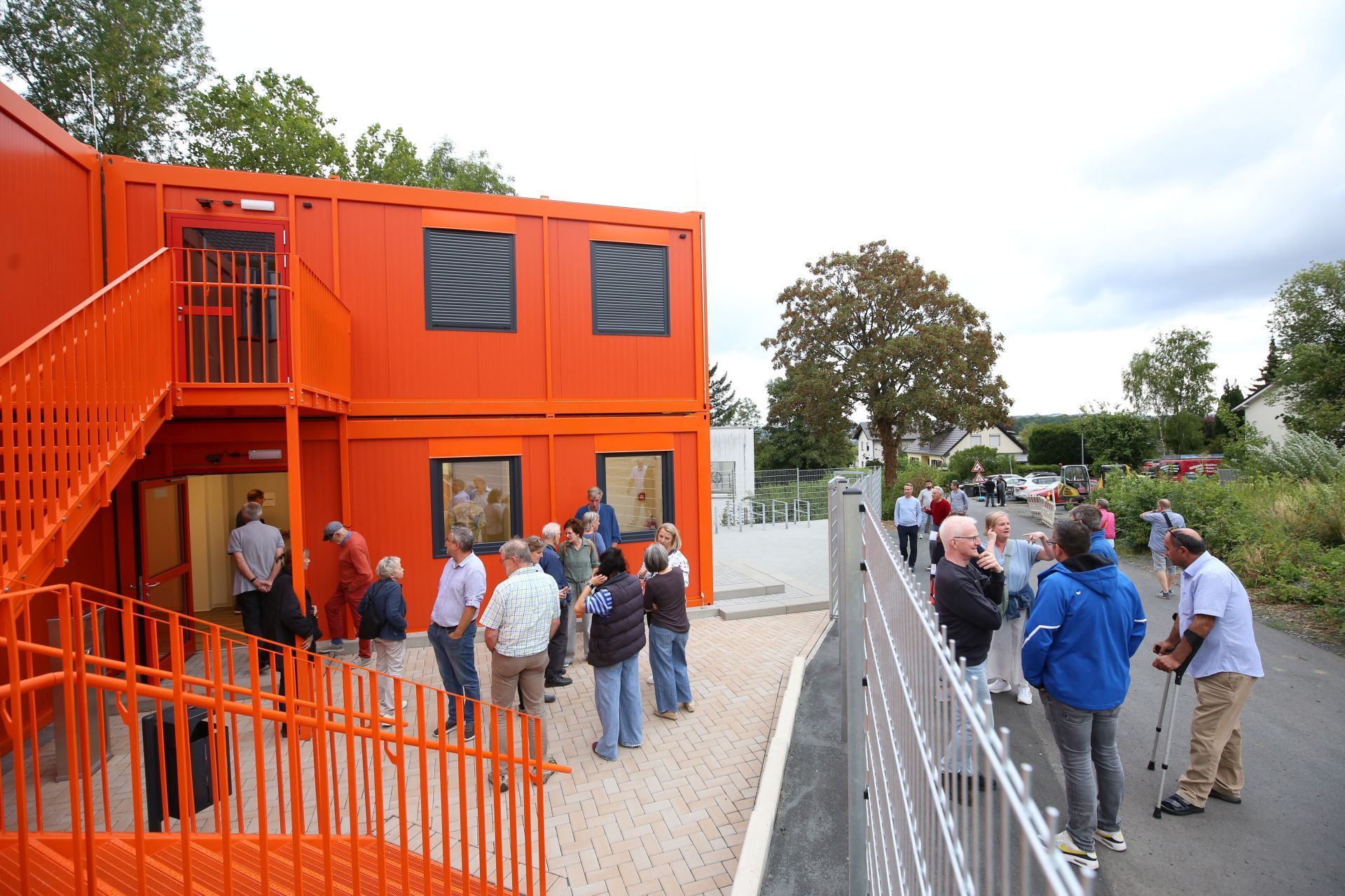 Mehrere Menschen vor Wohncontainern, deren Fassade orange gestrichen ist.