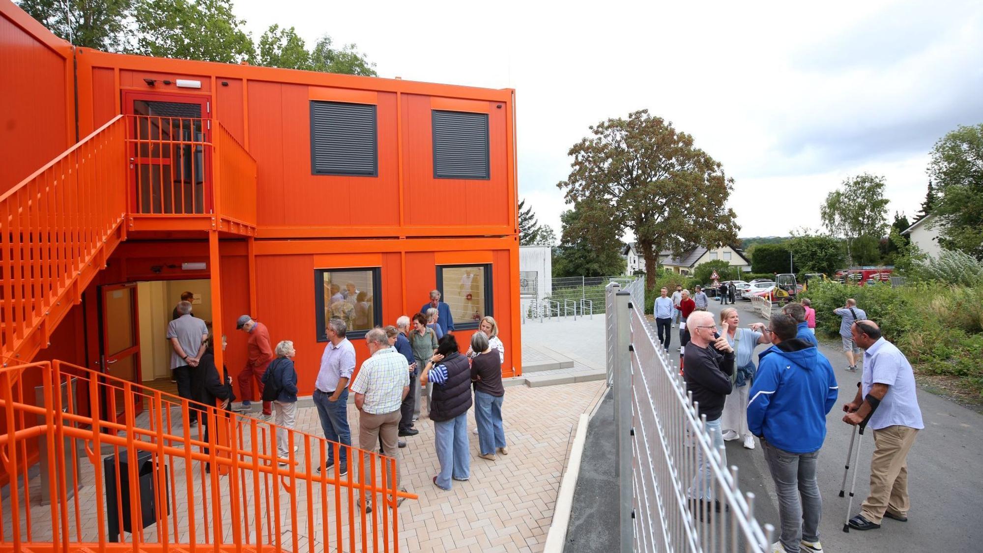 Mehrere Menschen vor Wohncontainern, deren Fassade orange gestrichen ist.