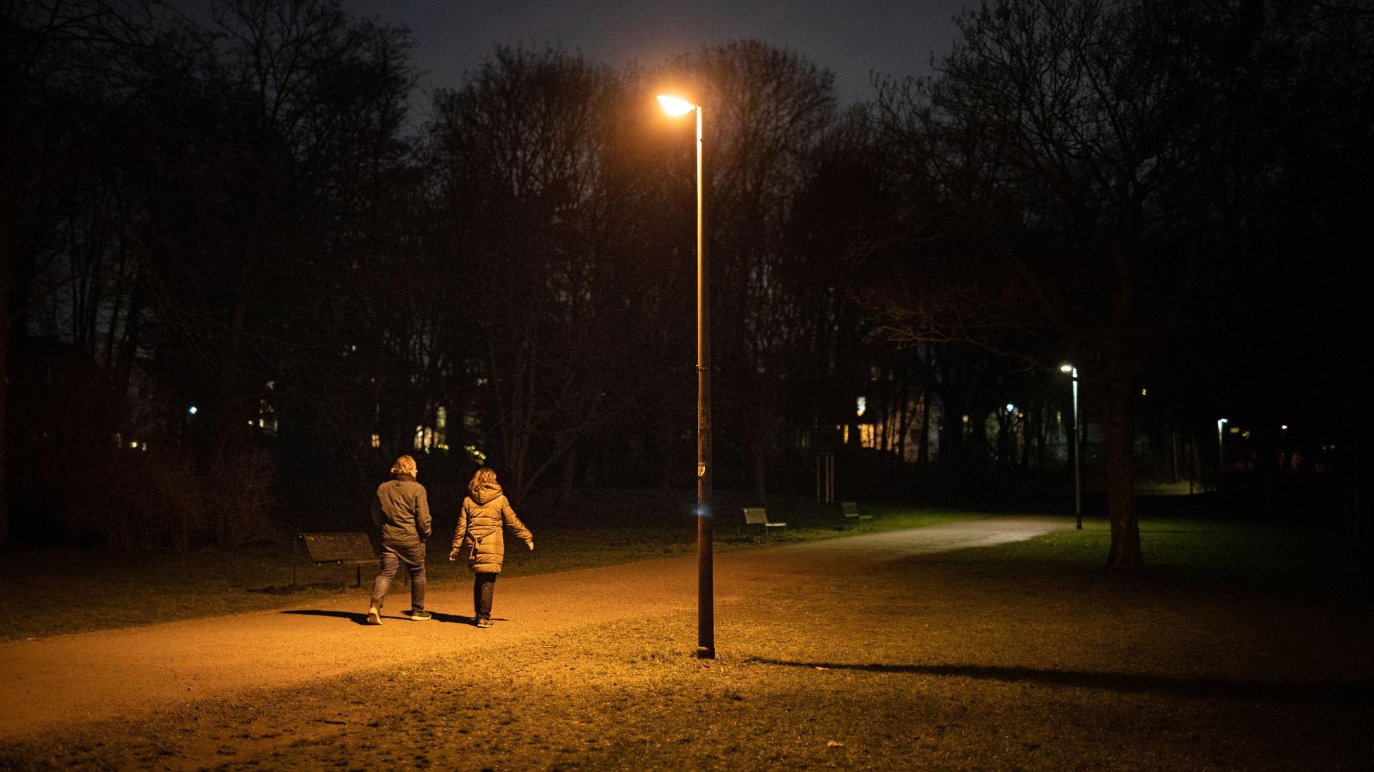 Zwei Personen sind am Abend auf einem Weg im dunklen Beethovenpark unterwegs, während eine Straßenlaterne leuchtet.
