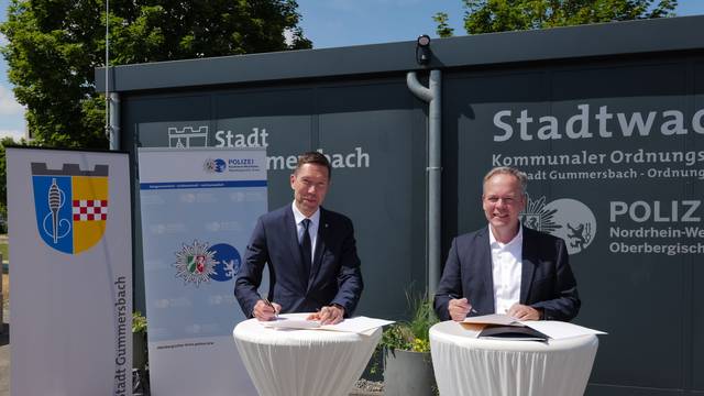 Zwei Männer stehen an Tischen und unterschreiben eine Kooperationsvereinbarung.