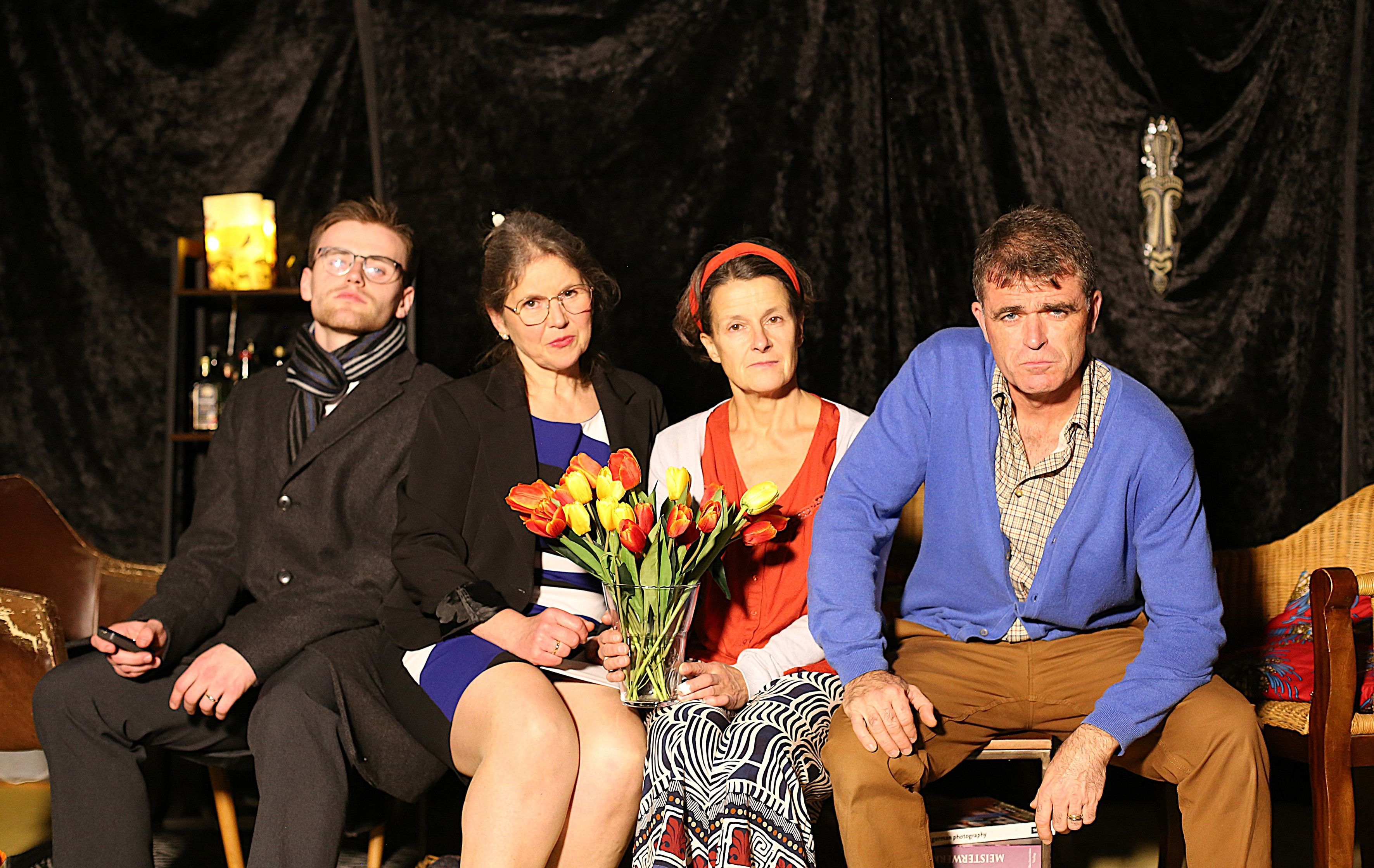 Zwei Schauspielerinnen und zwei Schauspieler sitzen nebeneinander. Eine Frau hält einen Strauß künstlicher Blumen.