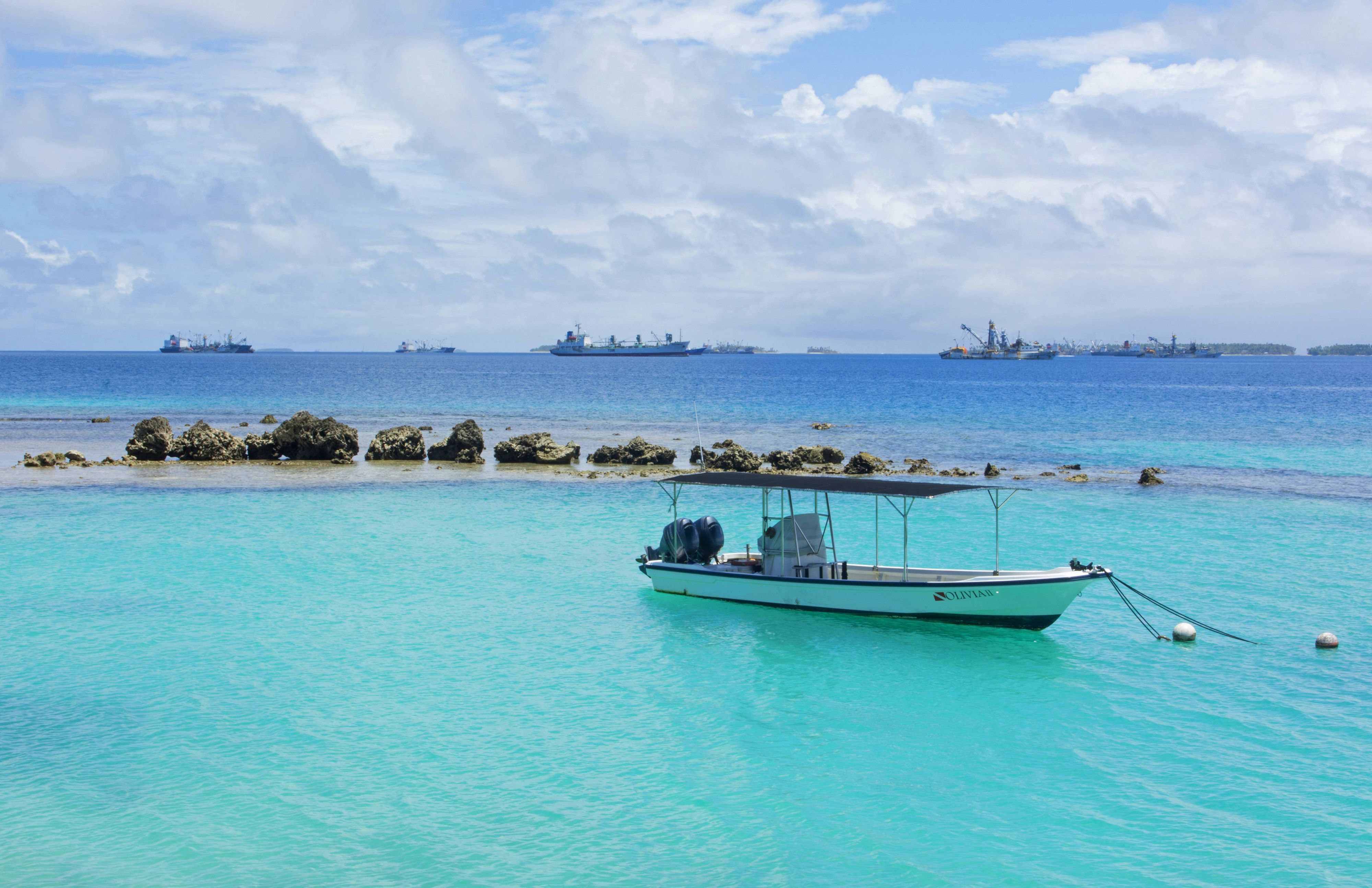 Vor Anker liegendes Boot mit Frachtschiffen im Hintergrund im Majuro-Atoll auf den Marshallinseln.
