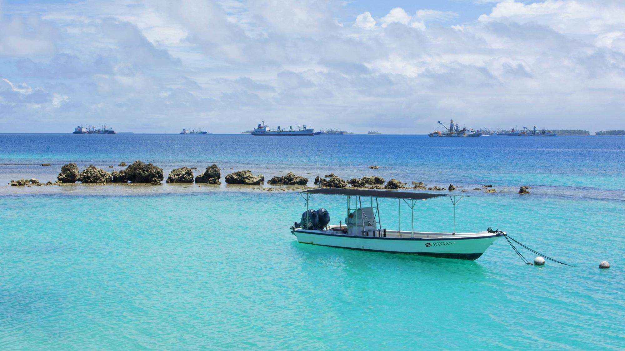 Vor Anker liegendes Boot mit Frachtschiffen im Hintergrund im Majuro-Atoll auf den Marshallinseln.