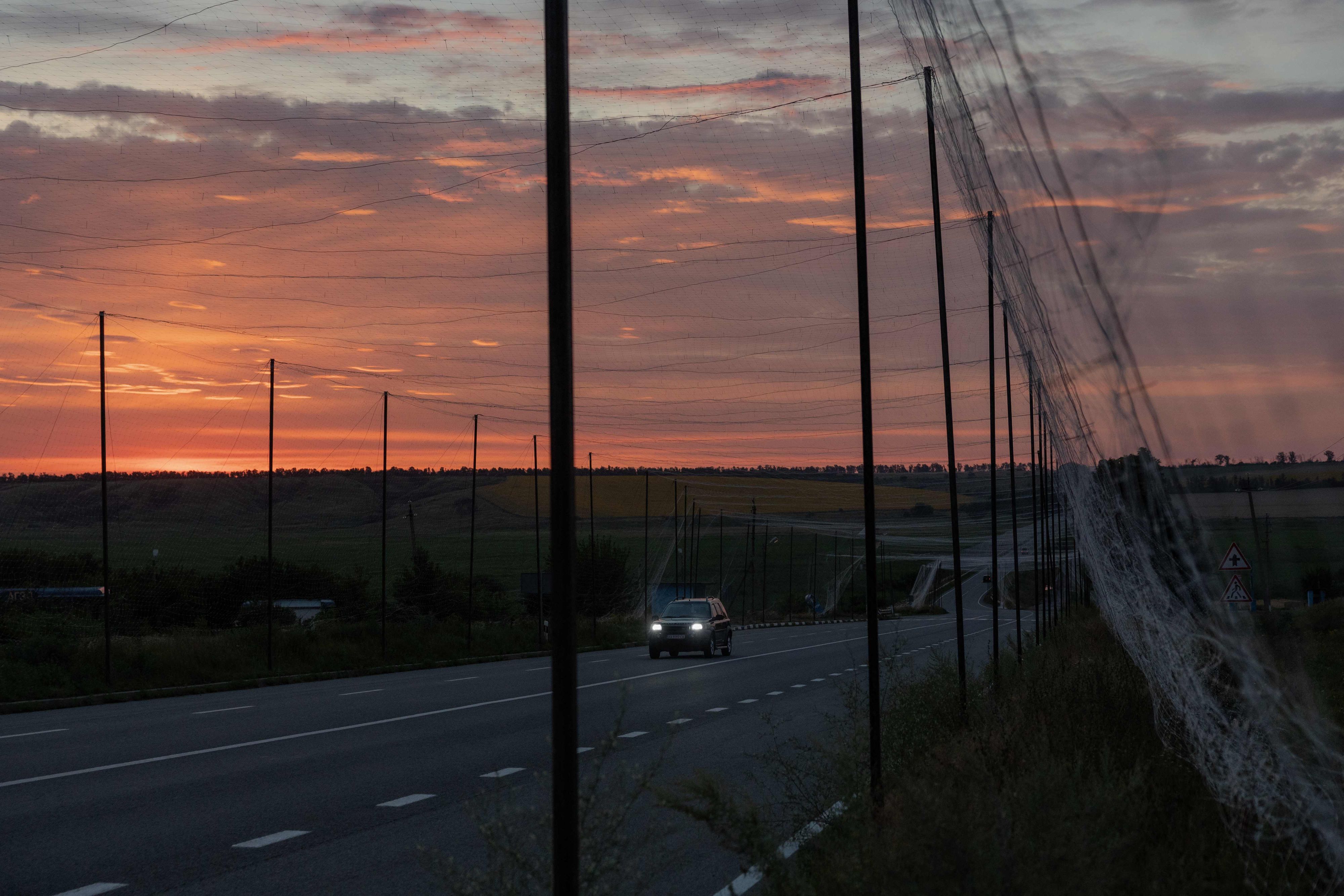 Ein Auto fährt in der ostukrainischen Region Charkiw auf einer Straße, die mit Schutznetzen gegen Drohnen überspannt ist. Die Aufnahme entstand während des russischen Angriffskriegs gegen die Ukraine.