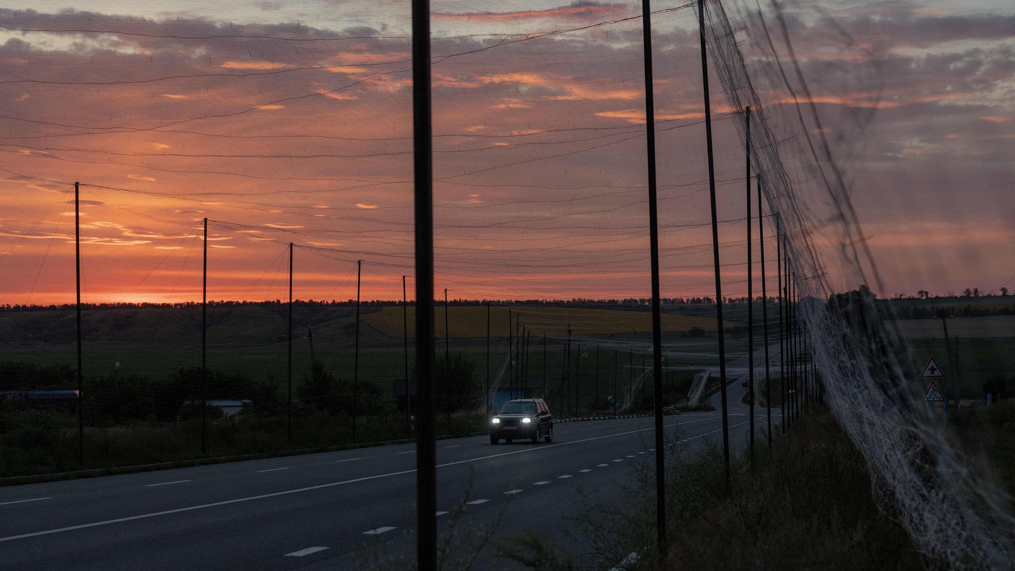 Ein Auto fährt in der ostukrainischen Region Charkiw auf einer Straße, die mit Schutznetzen gegen Drohnen überspannt ist. Die Aufnahme entstand während des russischen Angriffskriegs gegen die Ukraine.