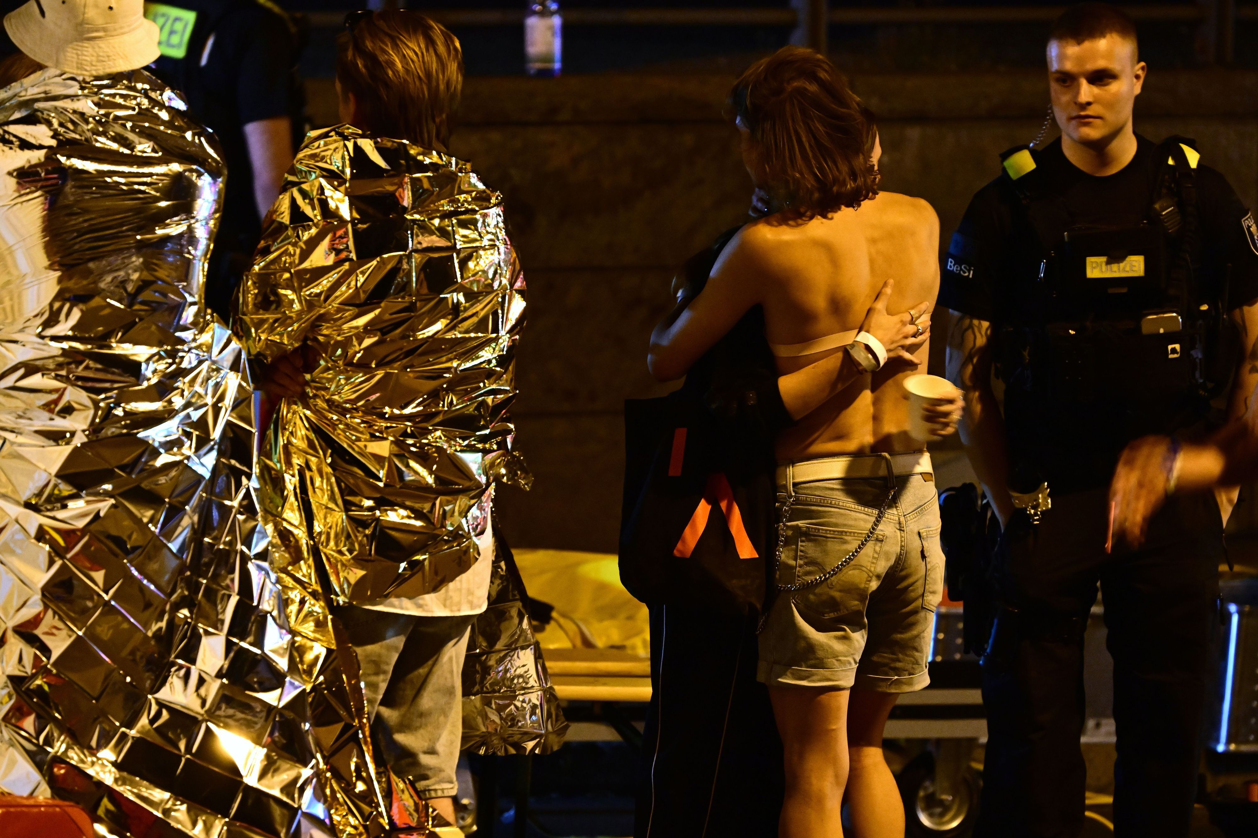 In Rettungsdecken gehüllte Personen stehen neben einem Zelt der Feuerwehr nach dem Abbruch des Christopher Street Day (CSD). Nachdem ein Auto mehrere Menschen am Rande der Feier in Berlin angefahren und verletzt hat, sucht die Polizei nach Verdächtigen.