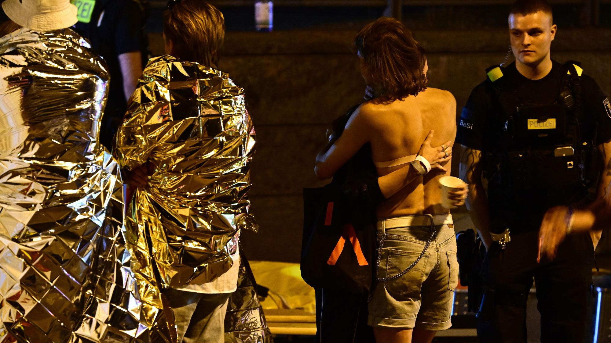 In Rettungsdecken gehüllte Personen stehen neben einem Zelt der Feuerwehr nach dem Abbruch des Christopher Street Day (CSD). Nachdem ein Auto mehrere Menschen am Rande der Feier in Berlin angefahren und verletzt hat, sucht die Polizei nach Verdächtigen.