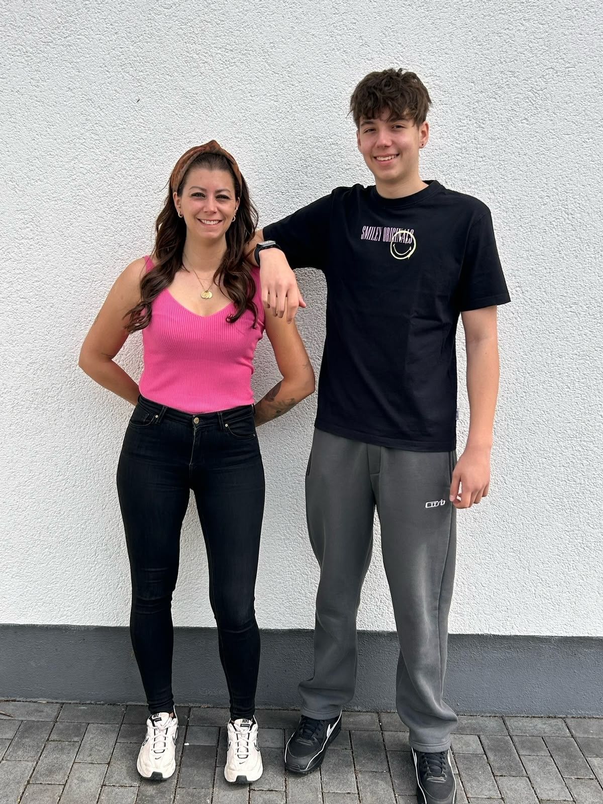 Mutter und Sohn stehen nebeneinander. Er hat einen Arm auf ihre Schulter gelegt.