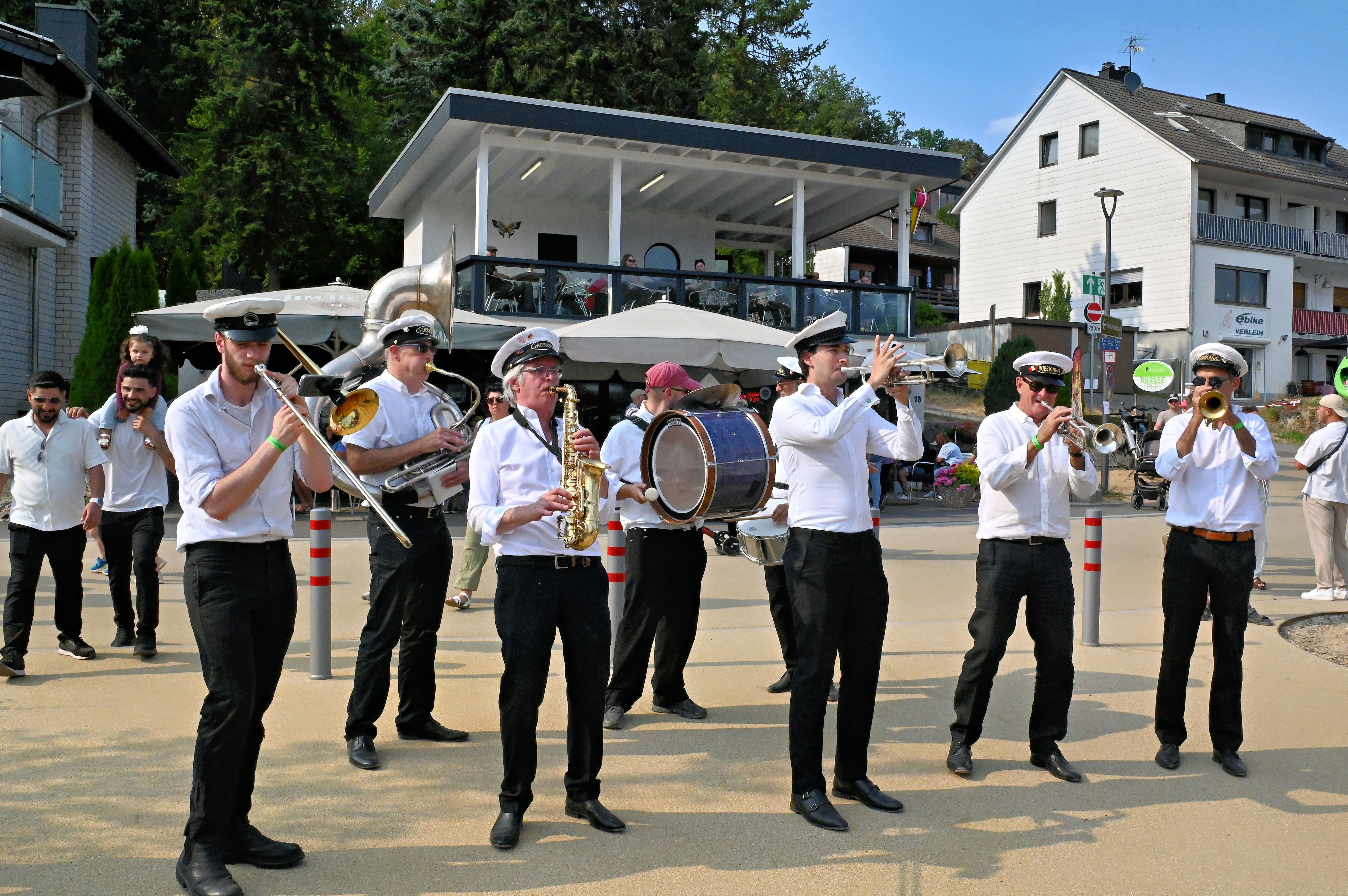 Männer in weiß-schwarzen Uniformen musizieren auf einem Platz.