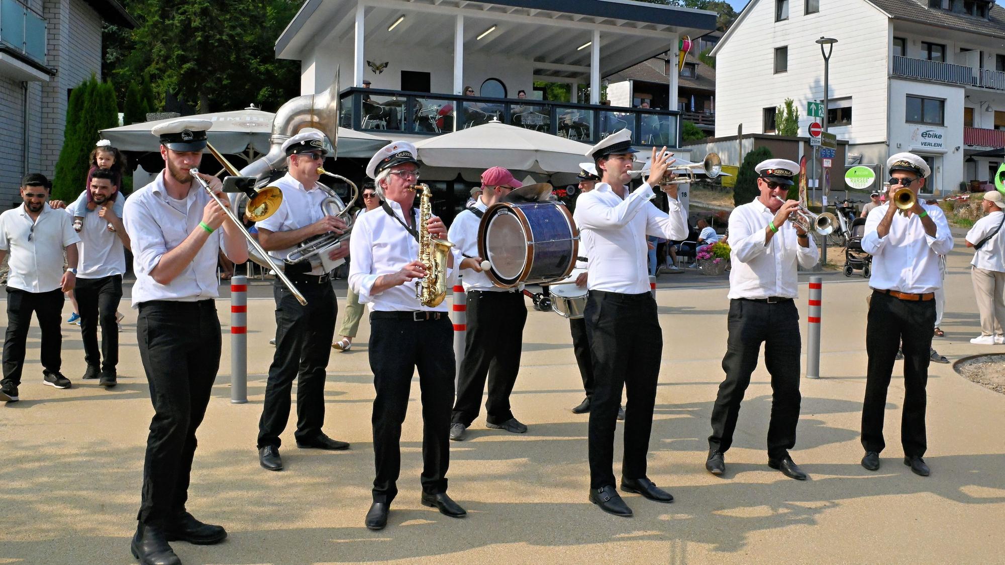 Männer in weiß-schwarzen Uniformen musizieren auf einem Platz.