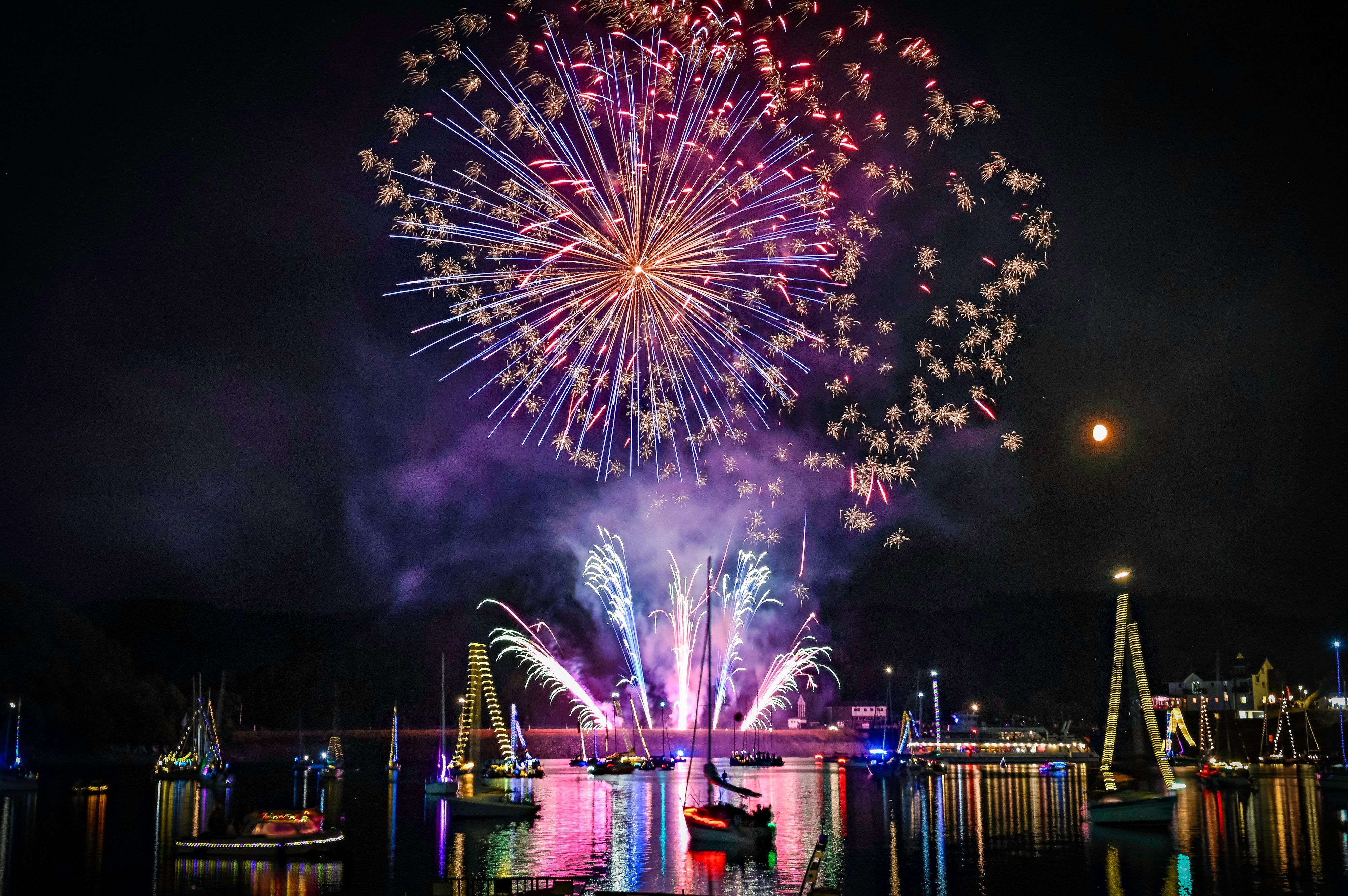 Das Feuerwerk spiegelt sich auf der Wasseroberfläche, auf der mit Lichtern geschmückte Boote schwimmen.