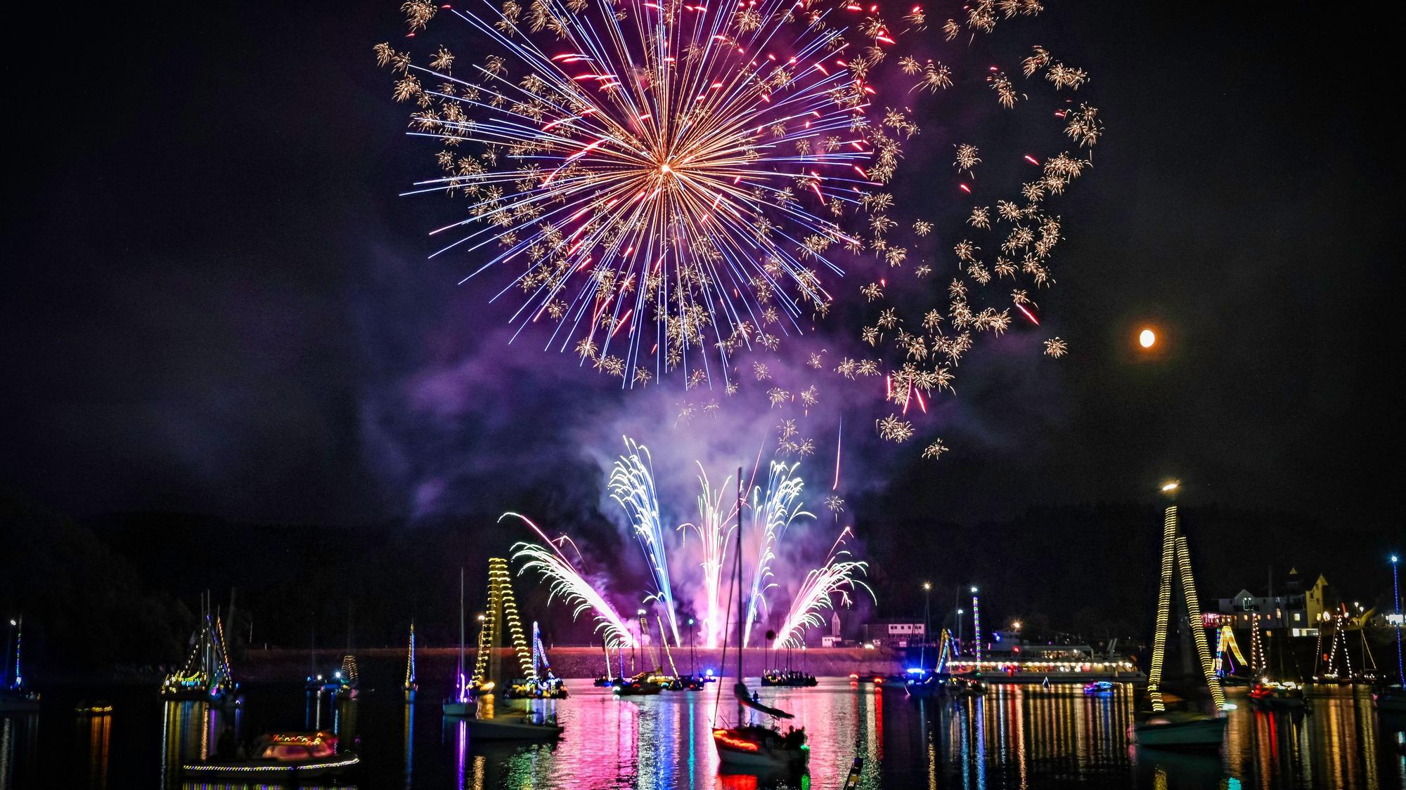 Das Feuerwerk spiegelt sich auf der Wasseroberfläche, auf der mit Lichtern geschmückte Boote schwimmen.
