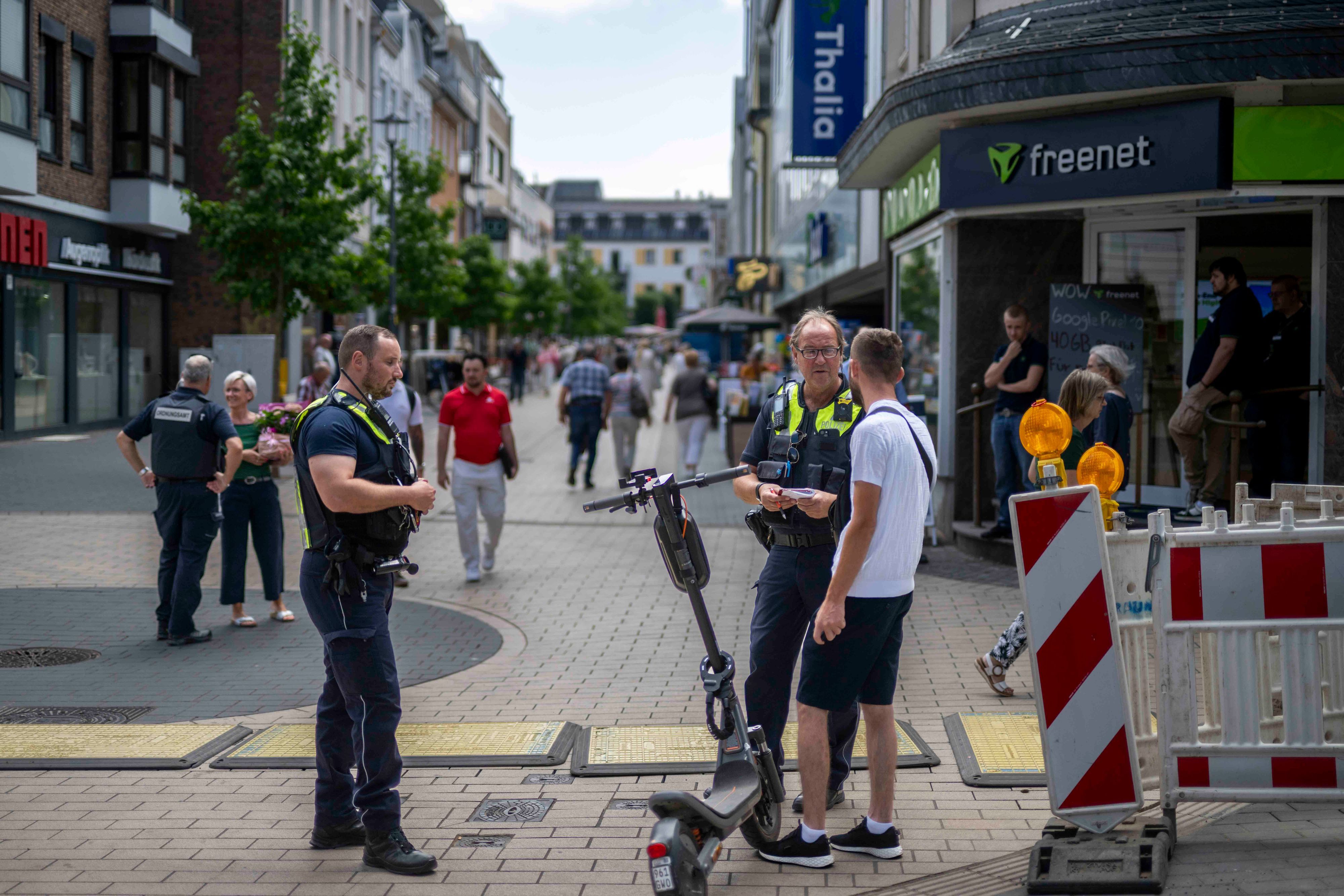 Das Bild zeigt einen Polizisten und einen Mitarbeiter des Euskirchener Ordnungsamts, wie sie gemeinsam einen E-Scooter-Fahrer kontrollieren.