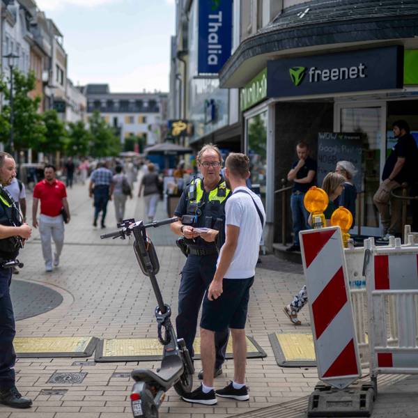 Das Bild zeigt einen Polizisten und einen Mitarbeiter des Euskirchener Ordnungsamts, wie sie gemeinsam einen E-Scooter-Fahrer kontrollieren.