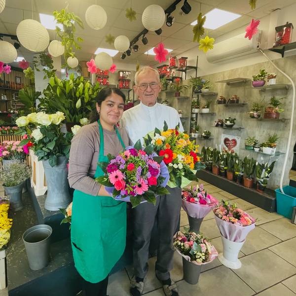 Eine junge Frau steht neben einem älteren Herrn in einem Blumenladen. Sie hält einen Strauß in der Hand.