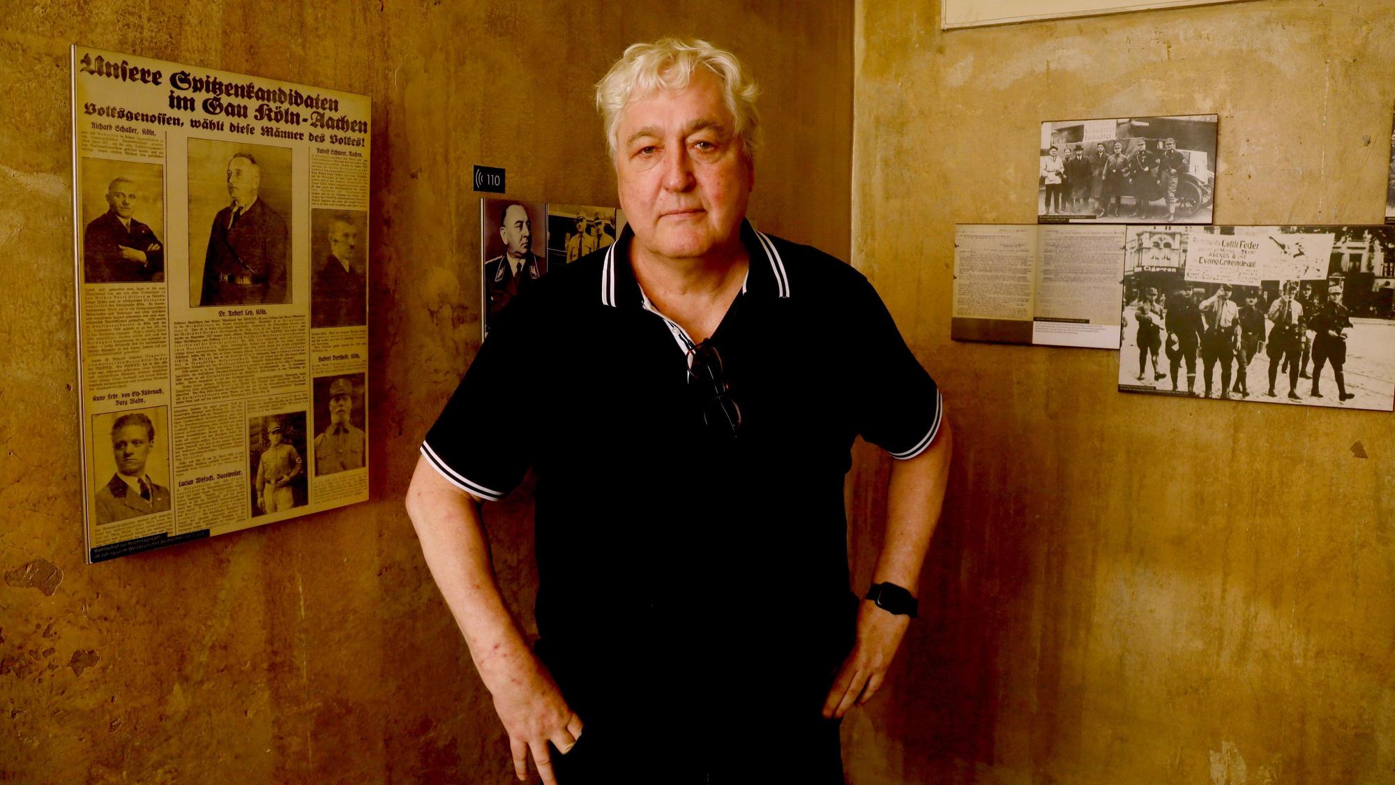 Der Journalist Axel Spilcker zu Besuch im NS-Dokumentationszentrum in Köln. An der Wand der Ausstellung hängt ein Artikel aus der NS-Zeit mit einem Foto seines Großvaters Robert Ley.