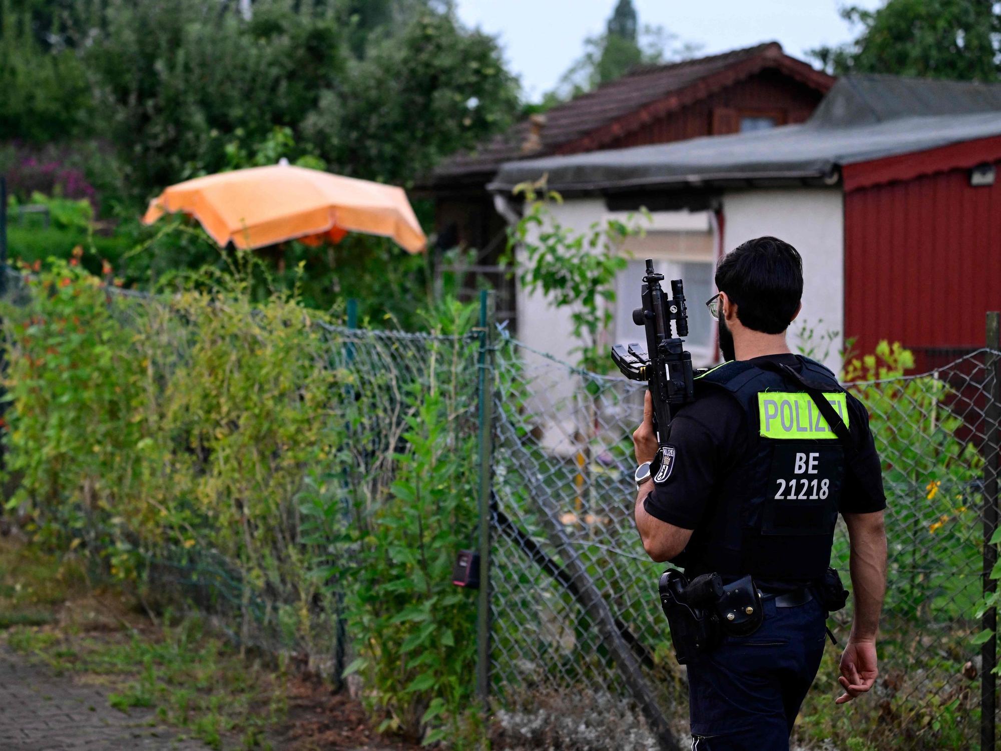 Ein Polizeibeamter mit einer automatischen Waffe geht am 26. Juli 2026 in einer Kleingartenanlage im Berliner Stadtteil Spandau durch einen Gartenbereich in der Nähe der Stelle, an der der Hauptverdächtige erschossen wurde.