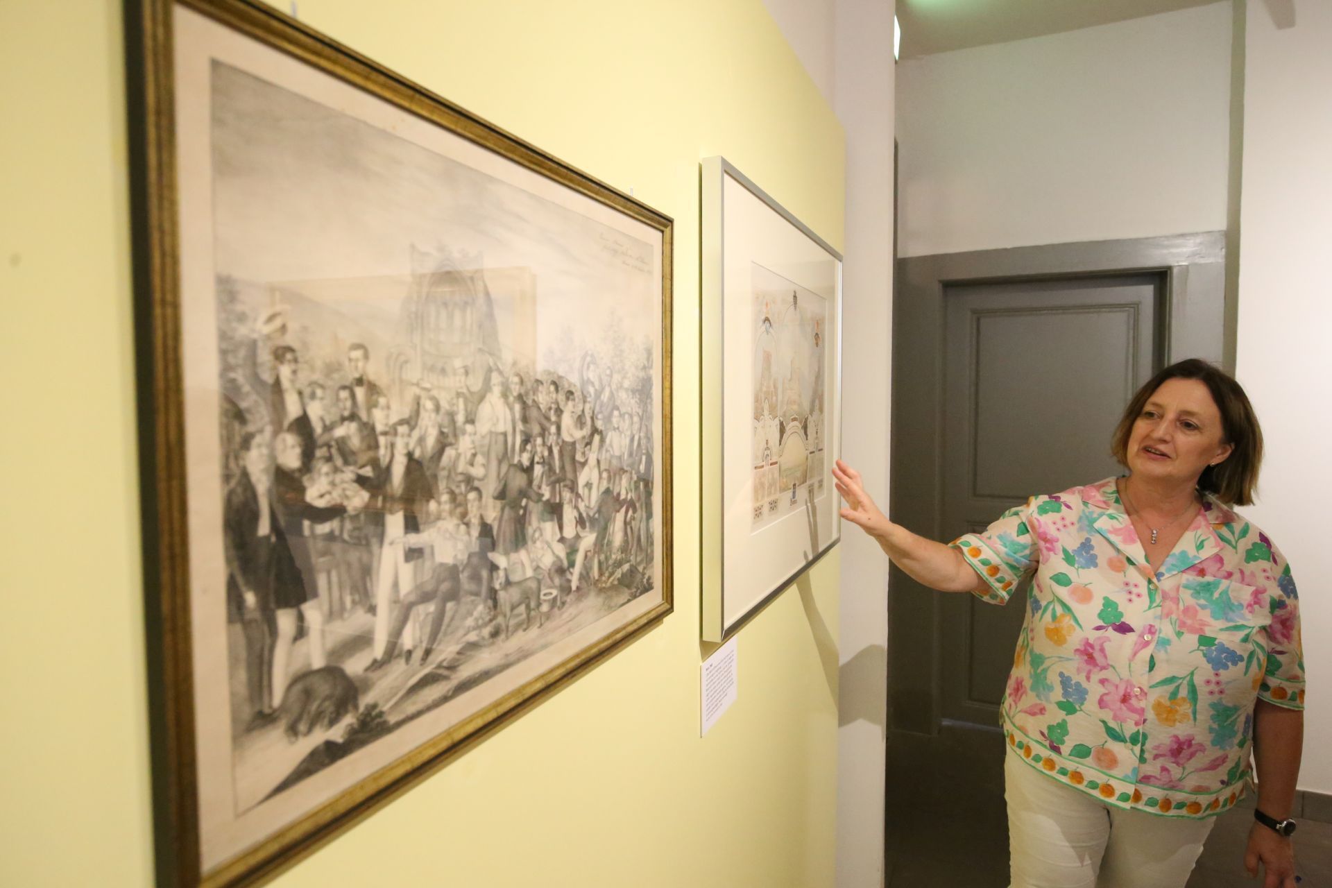 Eine Frau zeigt auf Bilder einer Ausstellung.