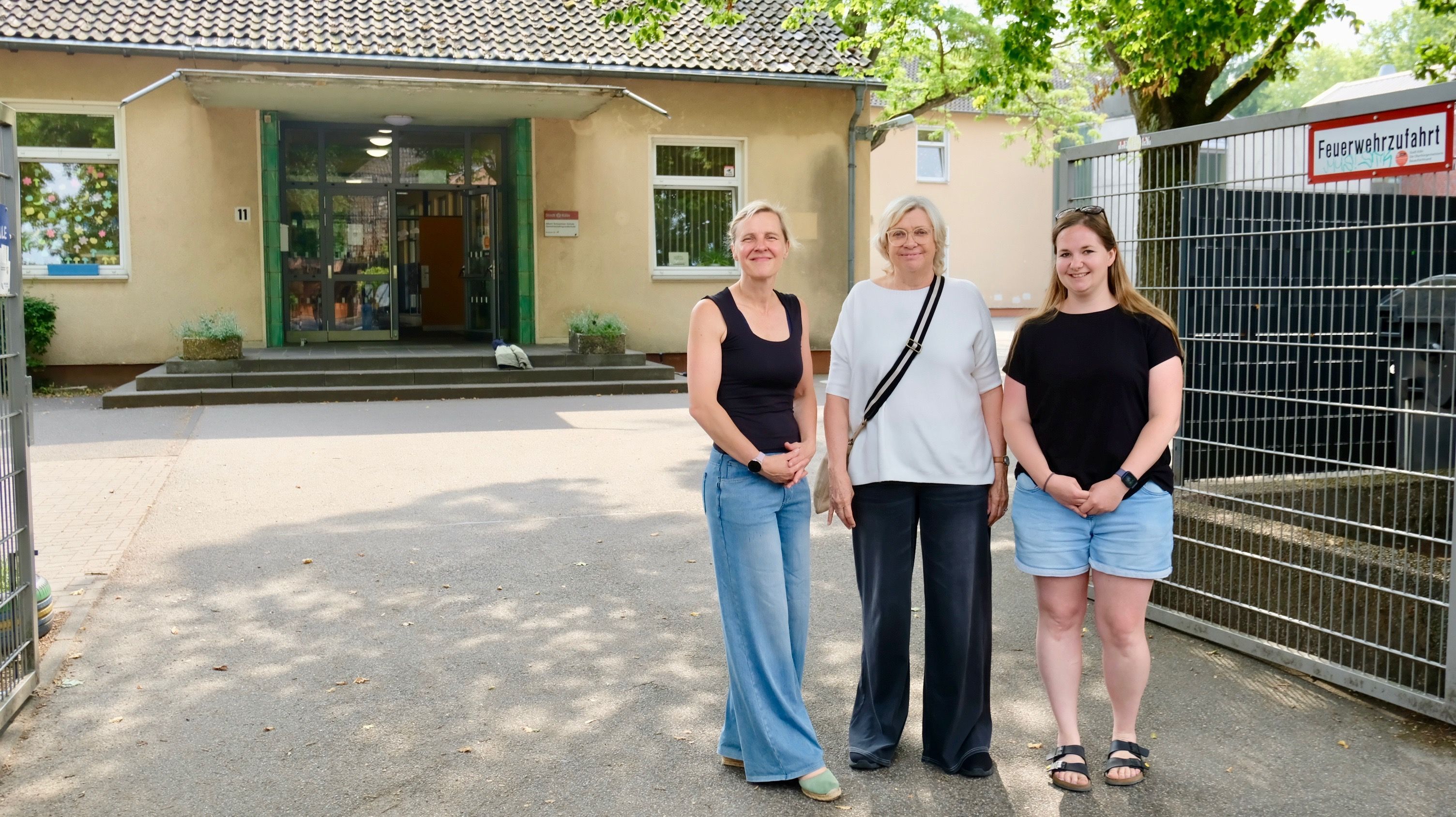 Drei Frauen stehen vor einem Schulgebäude.