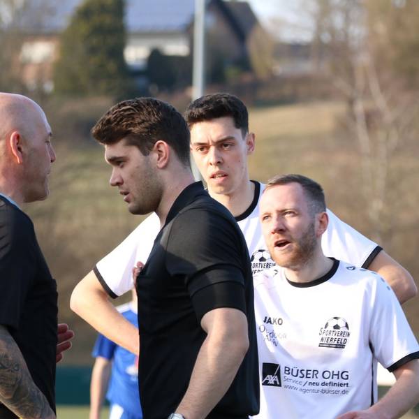 Das Bild zeigt zwei Schiedsrichter im Gespräch. Im Hintergrund diskutieren Fußballer. Es geht um eine sportliche Entscheidung während des Bezirksligaspiels.