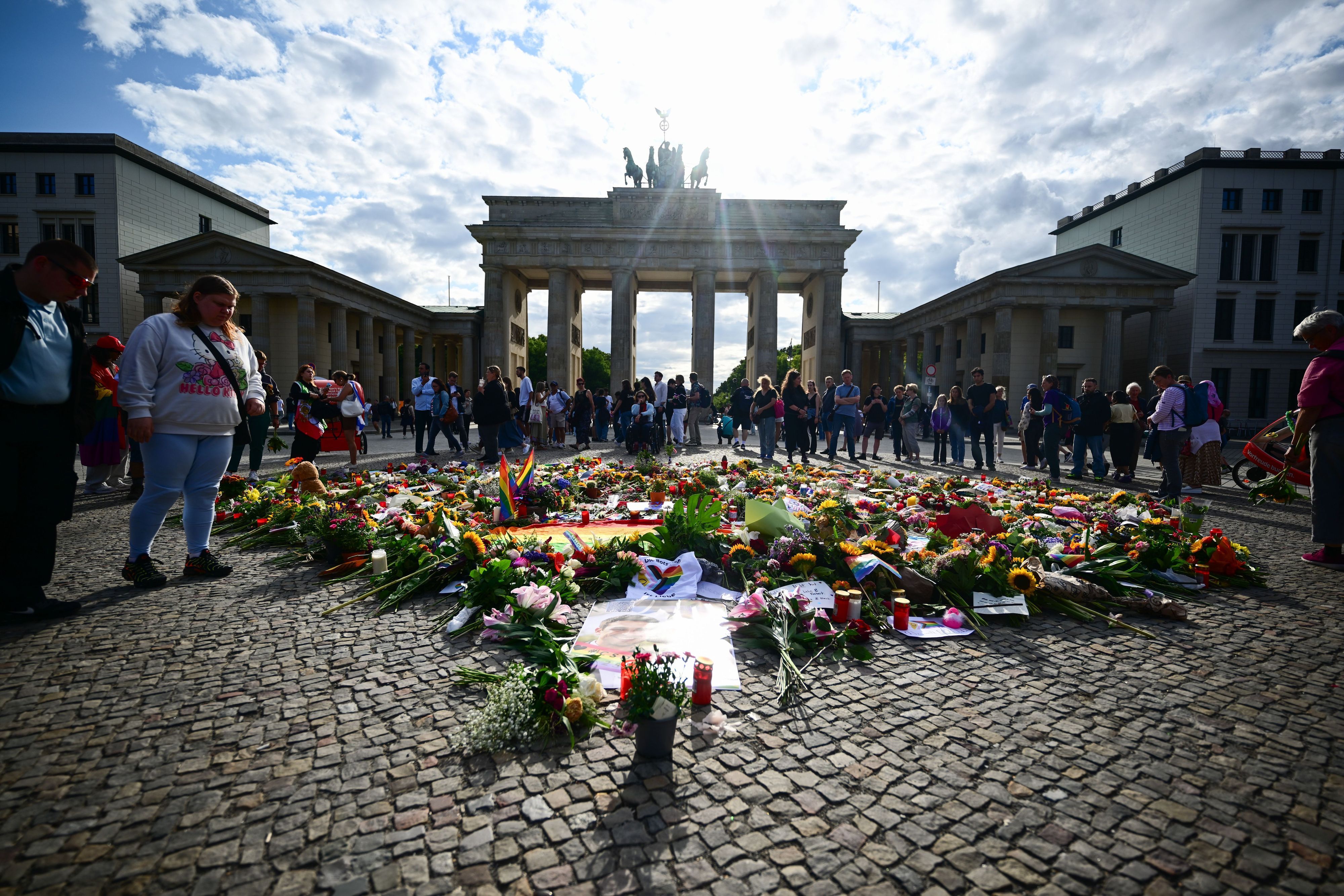 Menschen stehen an Beileidsbekundungen, Blumen, Flaggen und Kerzen, die vor dem Brandenburger Tor abgelegt wurden. Im Tiergarten war am Rande des Christopher Street Day ein Mann mit einem Fahrzeug in eine Menschenmenge gefahren.