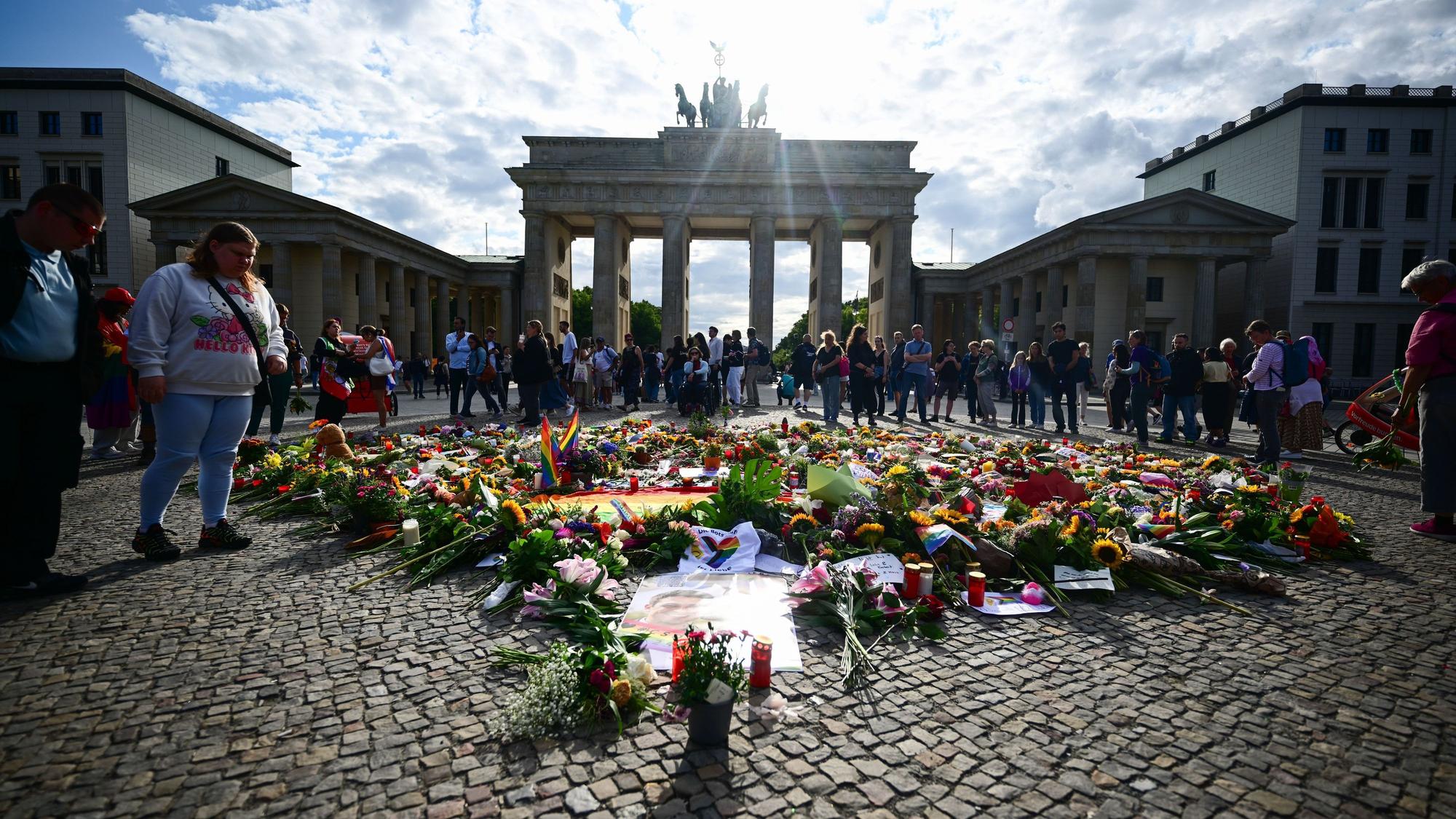 Menschen stehen an Beileidsbekundungen, Blumen, Flaggen und Kerzen, die vor dem Brandenburger Tor abgelegt wurden. Im Tiergarten war am Rande des Christopher Street Day ein Mann mit einem Fahrzeug in eine Menschenmenge gefahren.