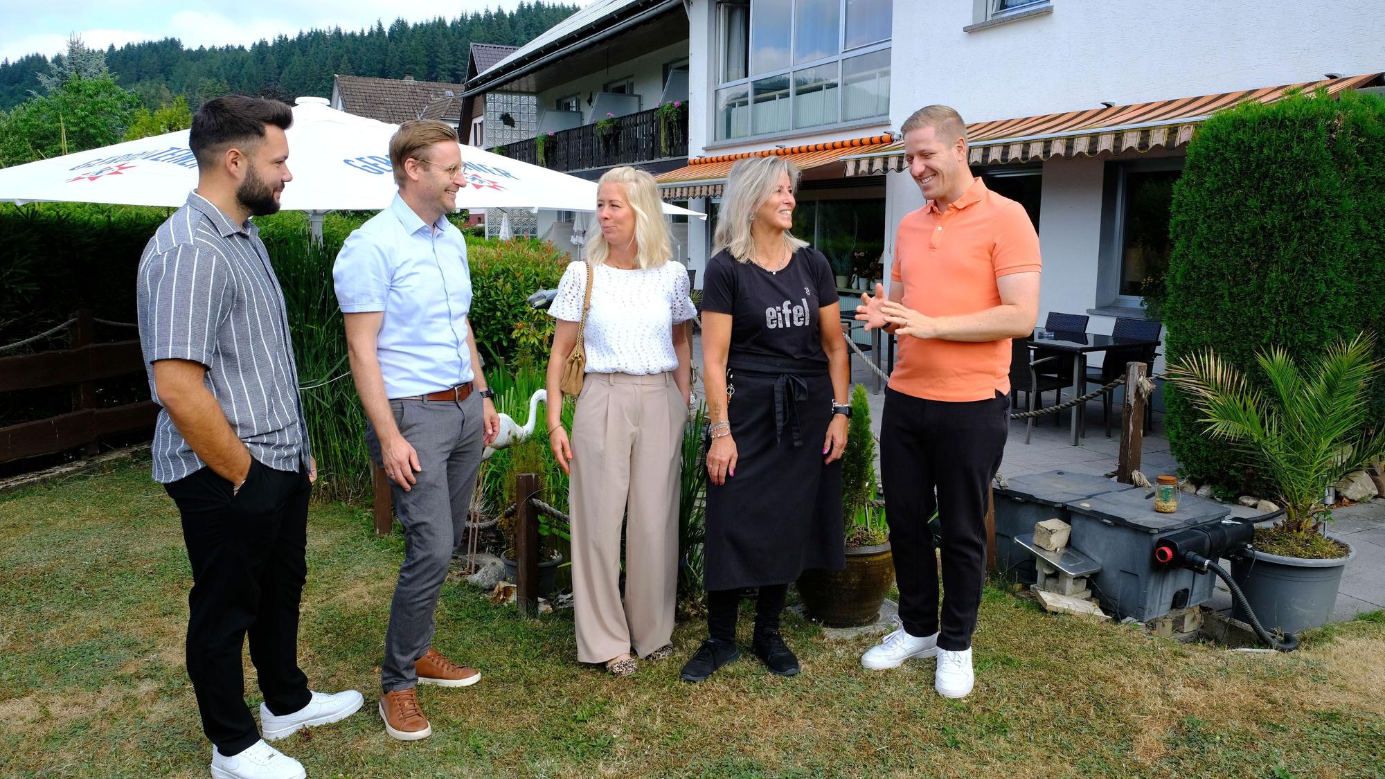 Die genannten Personen stehen im Garten vor dem Hellenthaler Hotel Berghof unter unterhalten sich miteinander.
