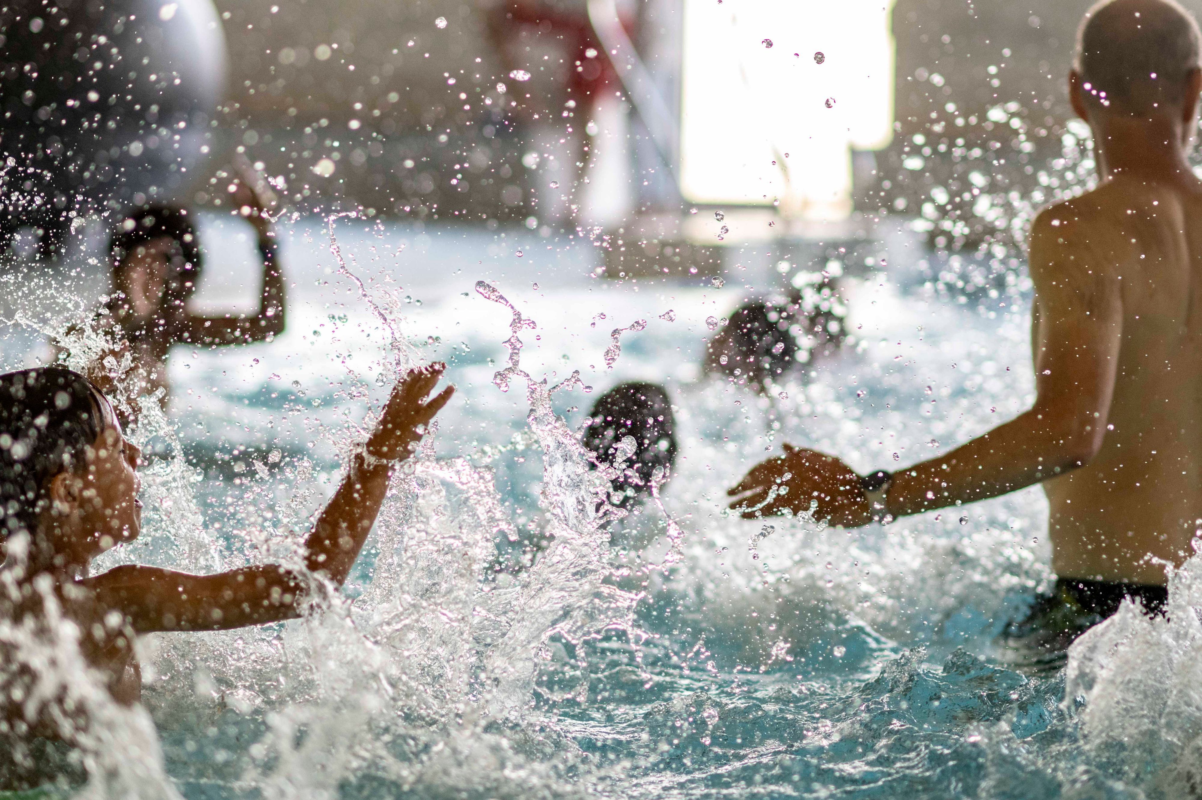 Das Bild zeigt zahlreiche Kinder und einen Schwimmlehrer, die im Wasser plantschen.