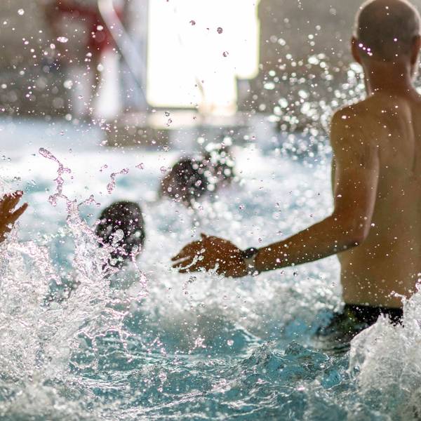 Das Bild zeigt zahlreiche Kinder und einen Schwimmlehrer, die im Wasser plantschen.