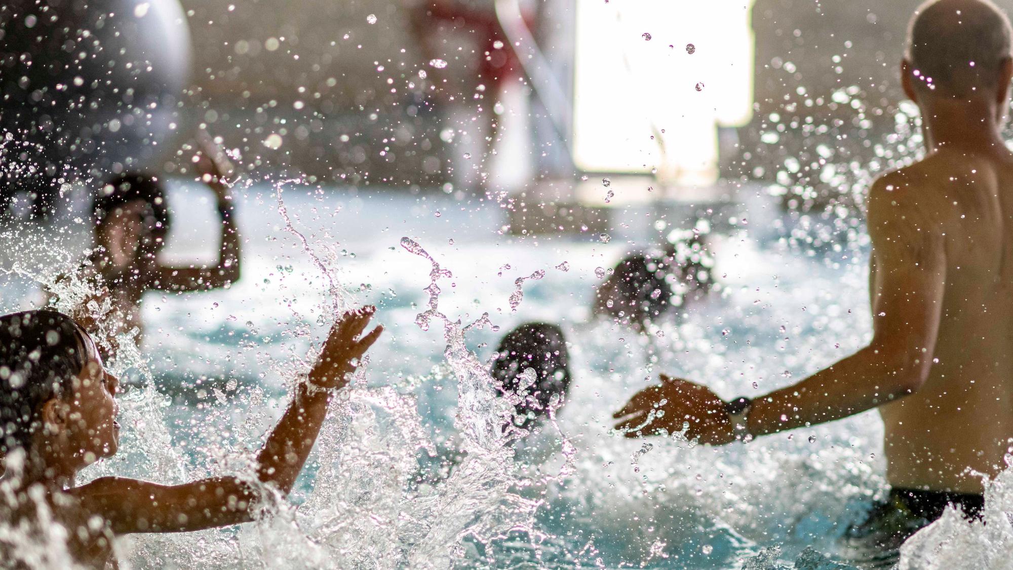 Das Bild zeigt zahlreiche Kinder und einen Schwimmlehrer, die im Wasser plantschen.