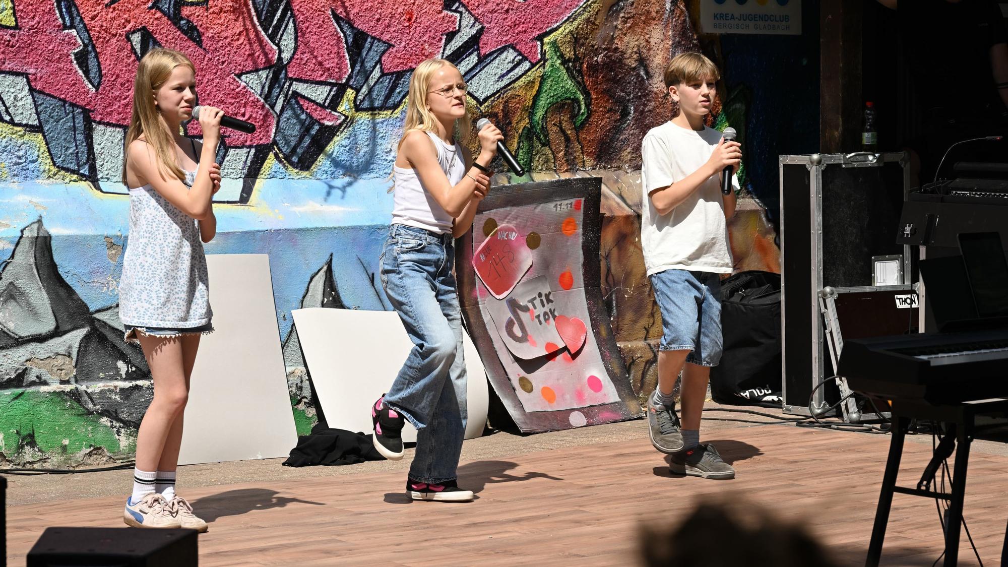 Zwei Mädchen und ein Junge singen in Mikrofone.