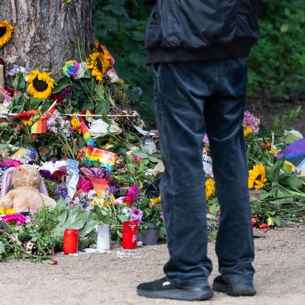 Trauernde stehen im Berliner Tiergarten an einem Baum, an dem unterschiedliche Gegenstände zum Gedenken an die Opfer des Anschlags auf den CSD abgelegt wurden.