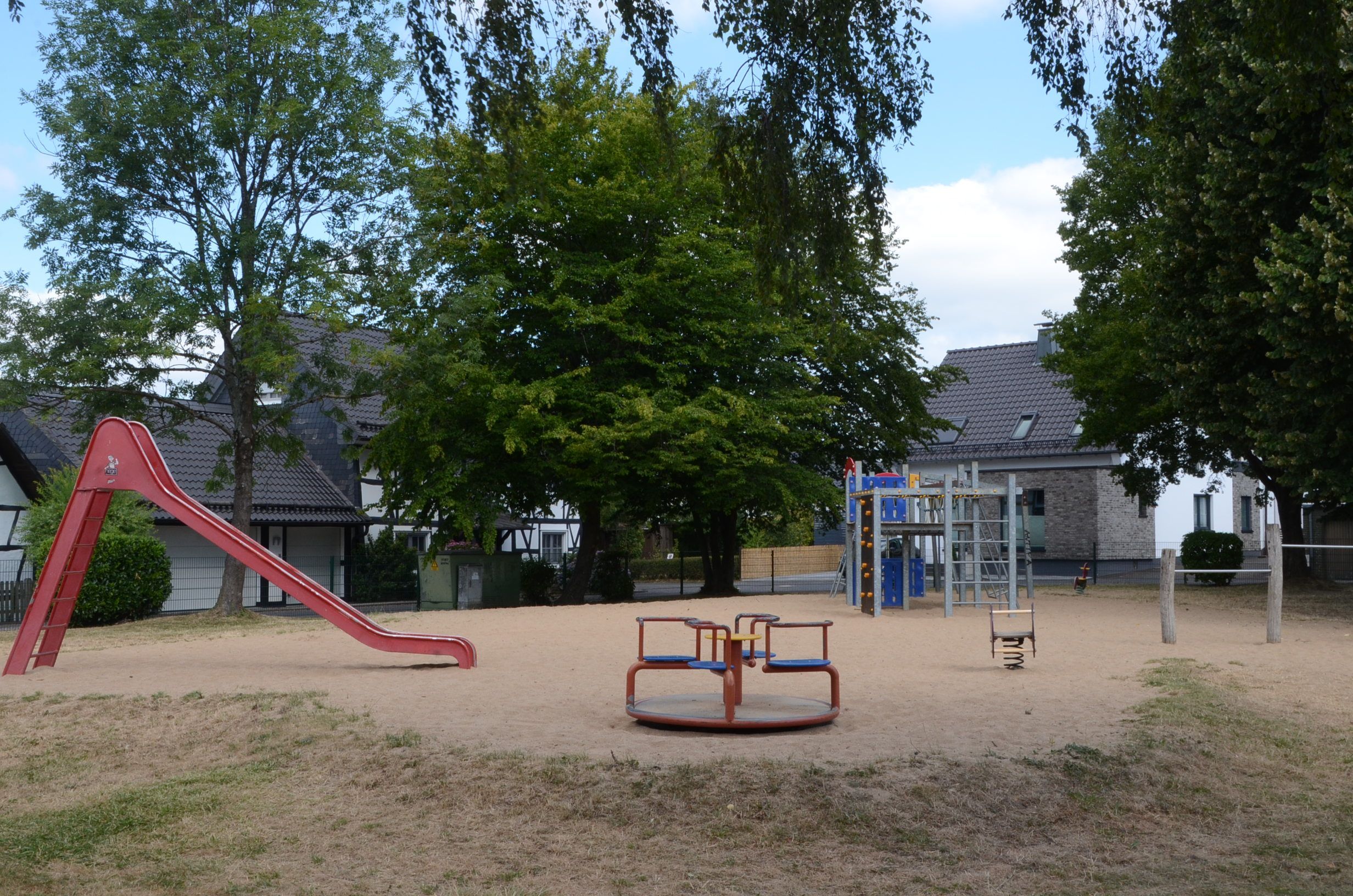 Ein Spielplatz mit Rutsche, Klettergerüst und kleinem Karussell.