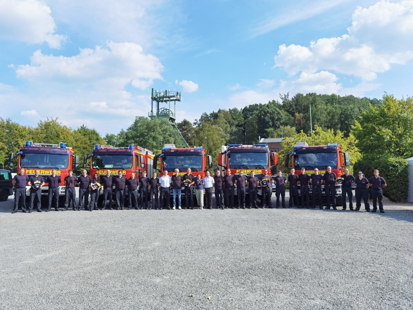 Zu sehen sind viele Feuerwehrleute aufgereiht nebeneinander. Hinter ihnen stehen fünf Feuerwehrwagen.