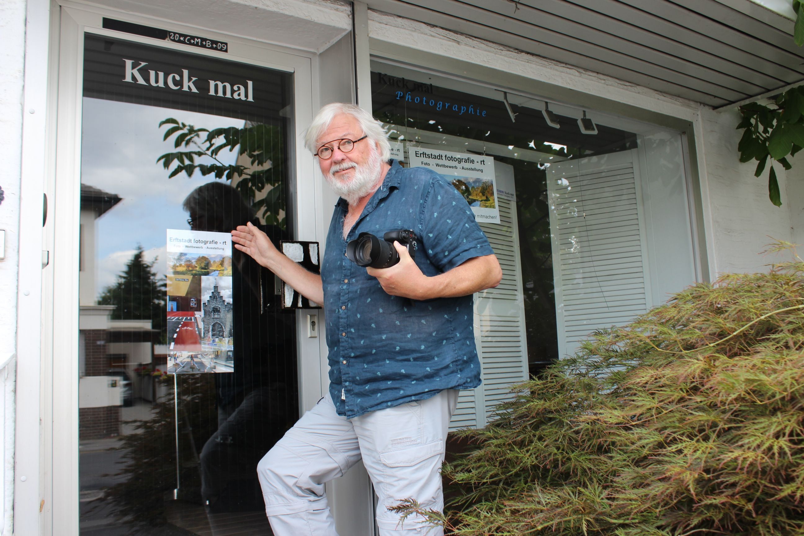 Das Bild zeigt den Fotografen, der seine Kamera hält, vor dem Kunstraum. Pber der Glastür hängt der Schriftzug „Kuck mal“.