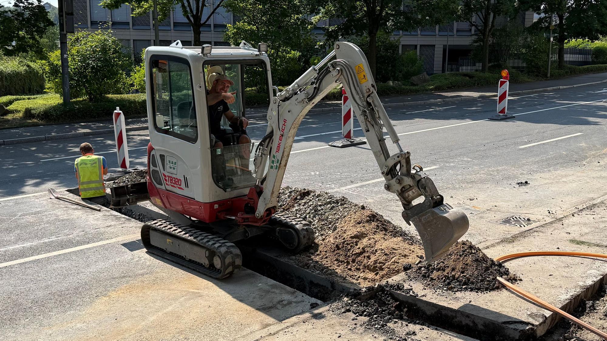Ein Arbeiter sitz im Bagger und arbeitet auf der Straße.