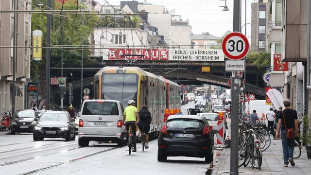 Das Foto zeigt die Luxemburger Straße auf Höhe der Eisenbahnbrücke Köln Süd. Die Straße wird genutzt von Straßenbahnen, Autos, Radfahrern und Fußgängern.