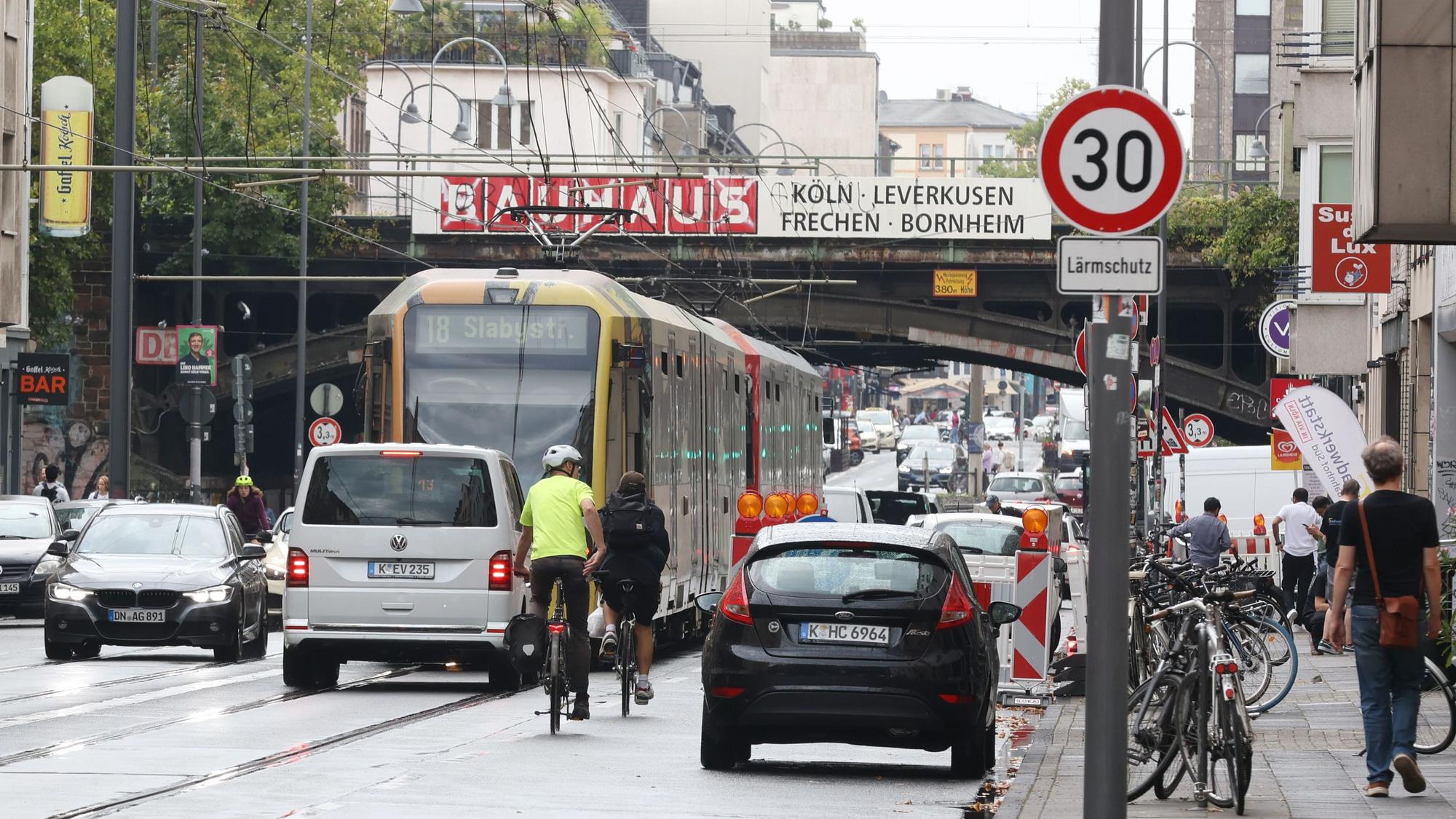 Das Foto zeigt die Luxemburger Straße auf Höhe der Eisenbahnbrücke Köln Süd. Die Straße wird genutzt von Straßenbahnen, Autos, Radfahrern und Fußgängern.