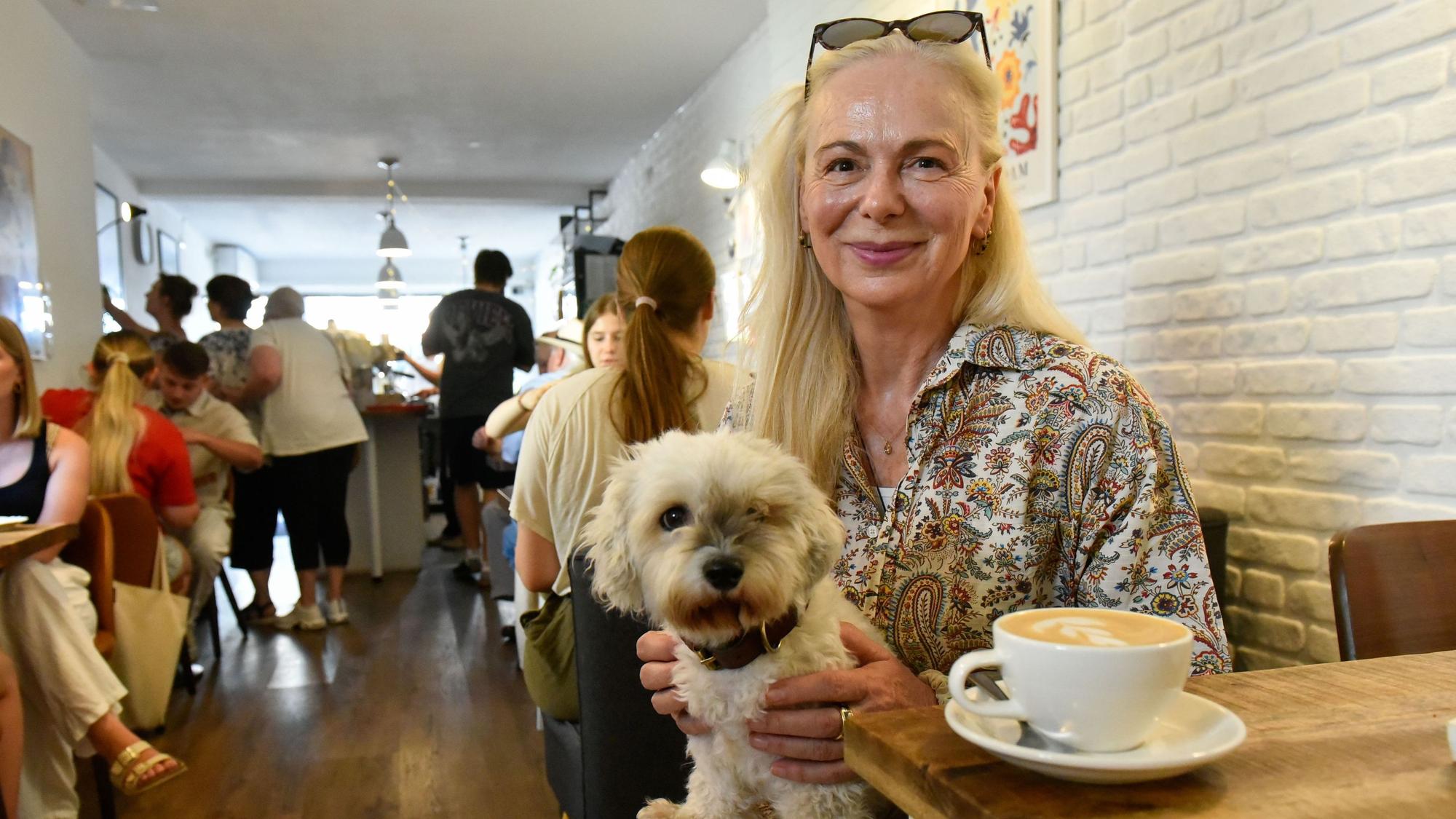 Eine Frau sitzt in einem Café, auf ihrem Schoß ein kleiner Hund.