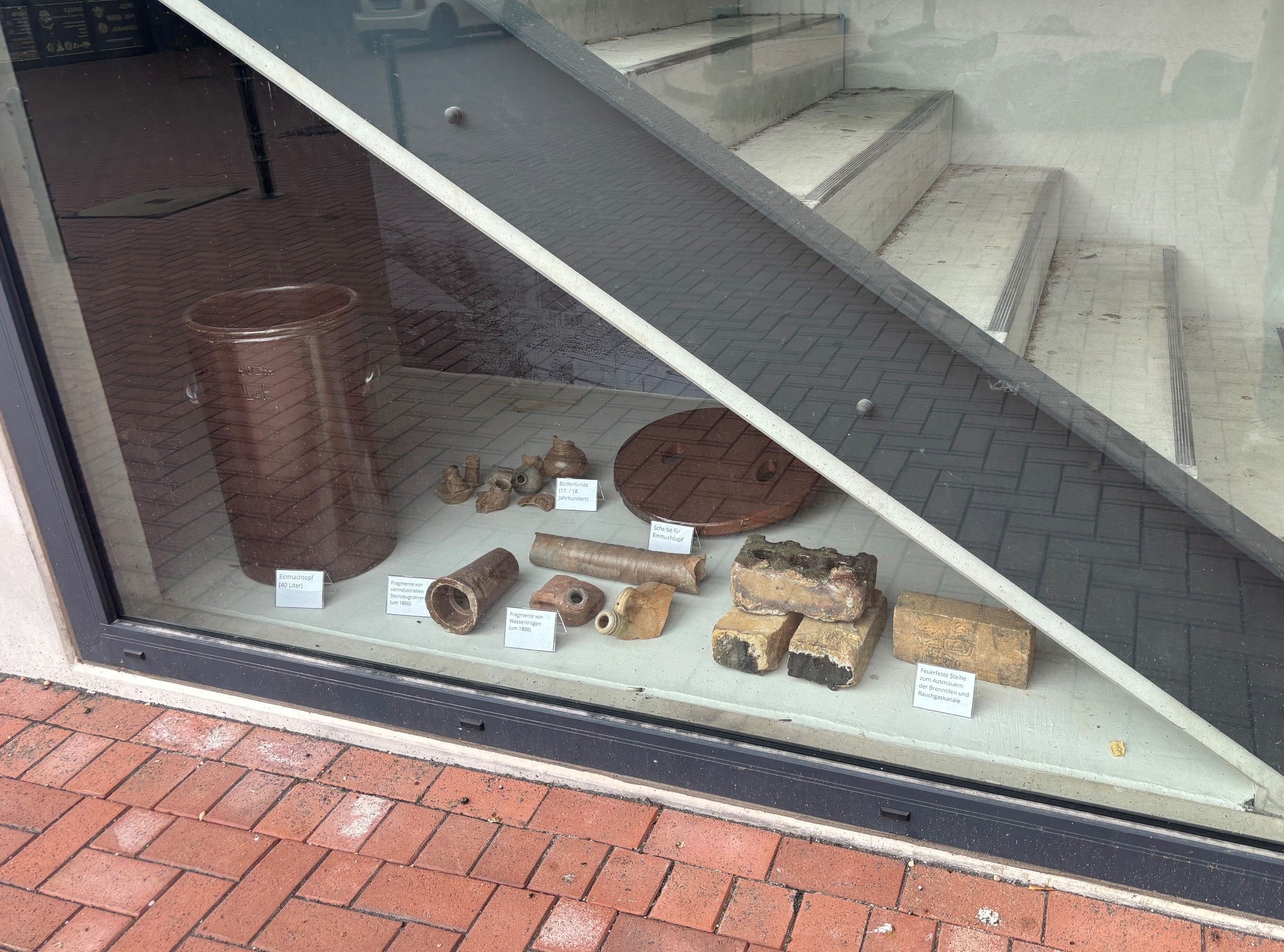 Durch ein Fenster sieht man eine Treppe und Ausstellungsstücke.