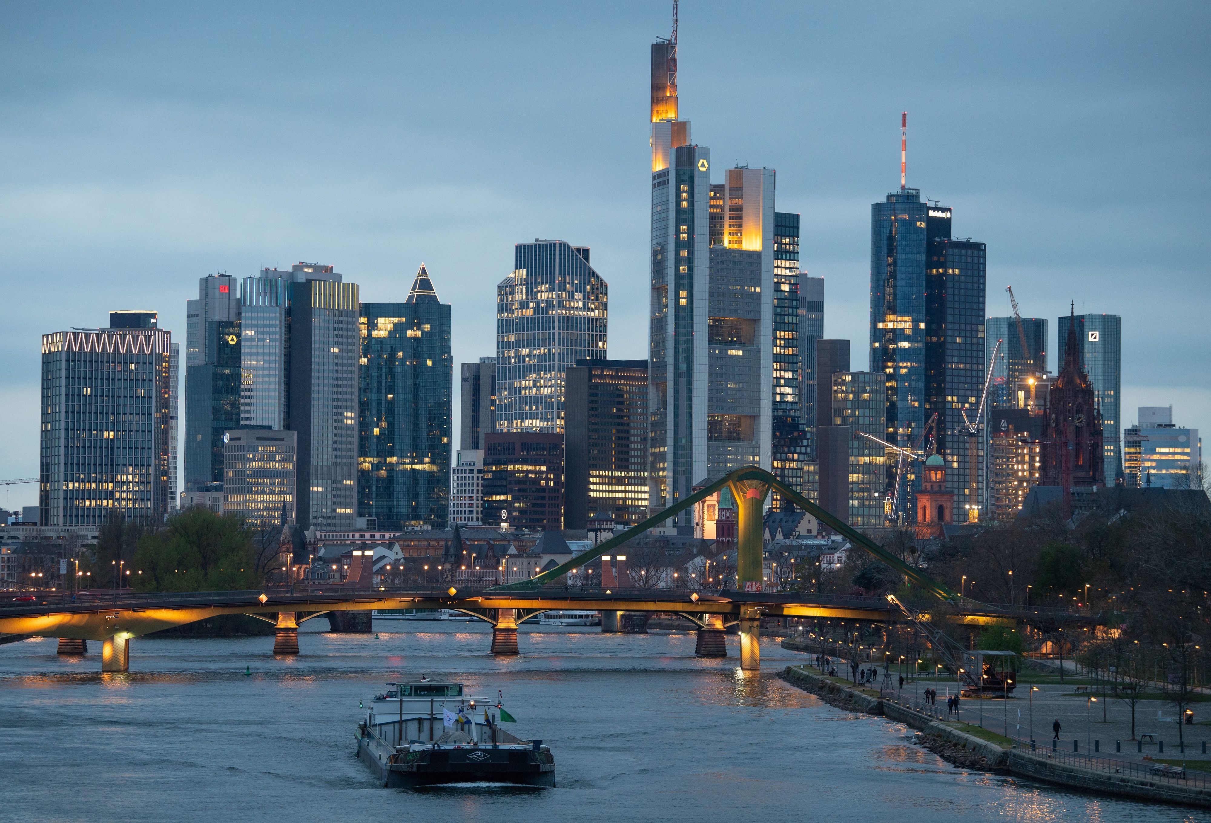 Binnenschiffe fahren im letzten Licht des Tages vor der Bankenskyline der Innenstadt über den Main