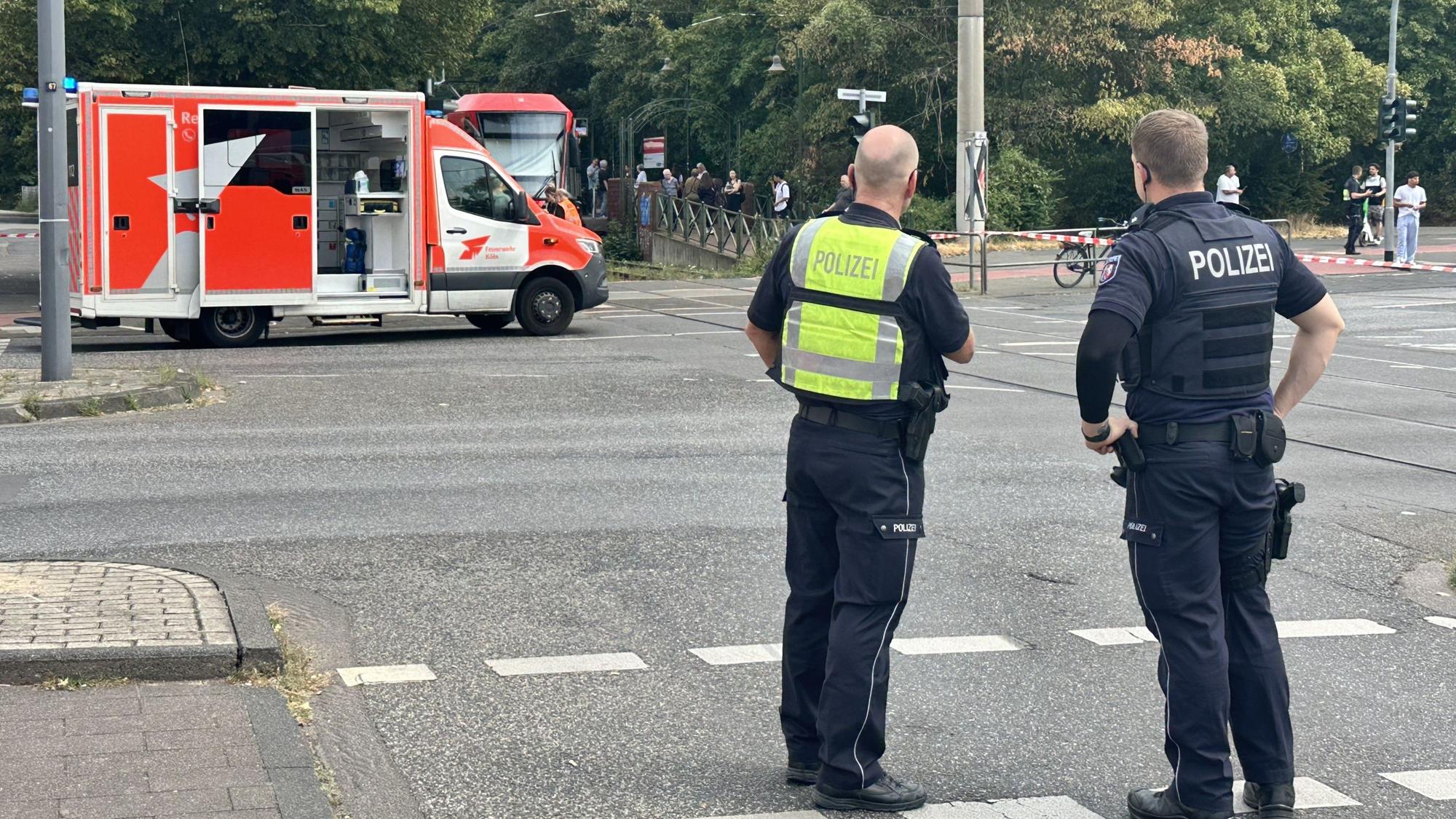 Zwei Polizisten stehen am Bahnübergang, dahinter ein Rettungswagen. Ein Unfallaufnahmeteam der Polizei ist in Köln-Buchheim vor Ort.