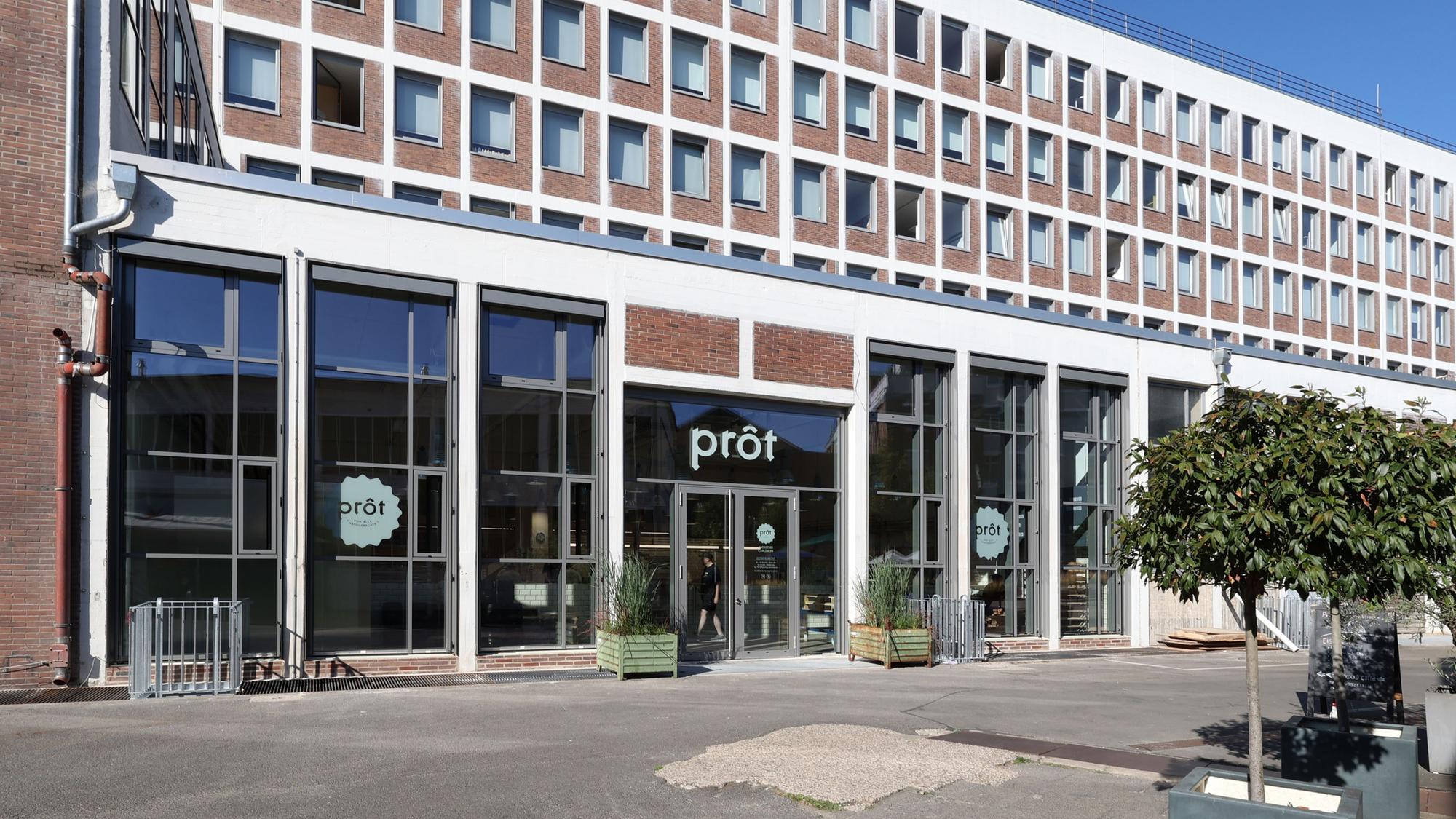 Auf der Glasfront eines Gebäudes prangt der Schriftzug Prôt.