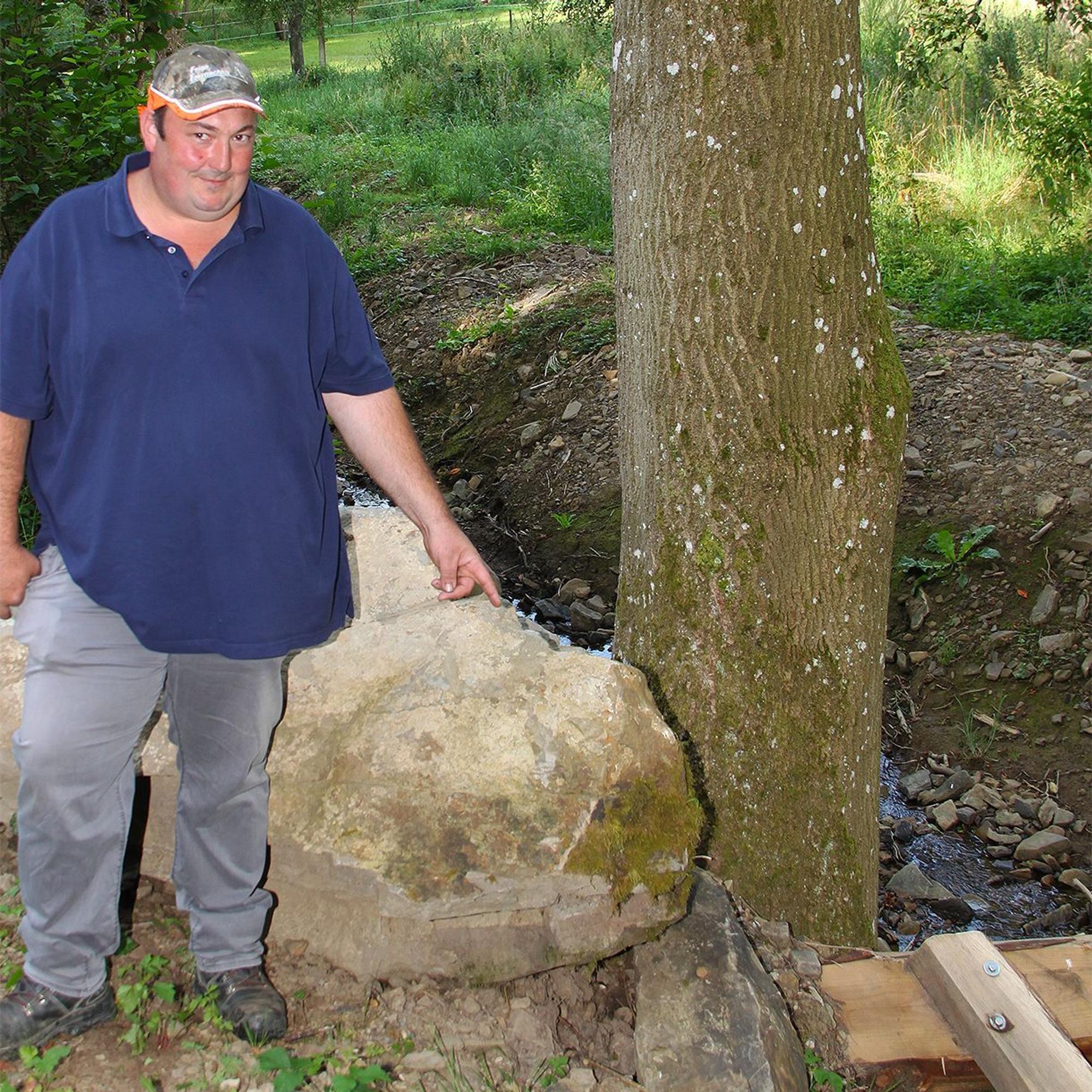 Der Baggerfahrer zeigt auf einen Wasserbaustein an einem Bachlauf.