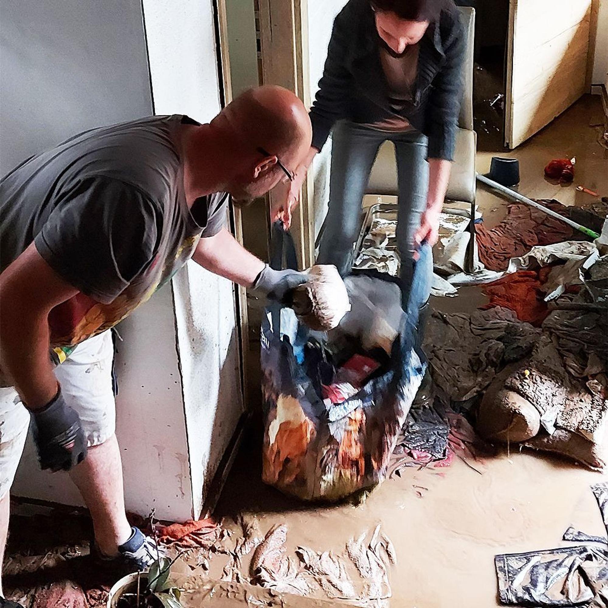 Ein Mann und eine Frau stehen im Schlamm und räumen zerstörte Untensilien aus dem Haus.