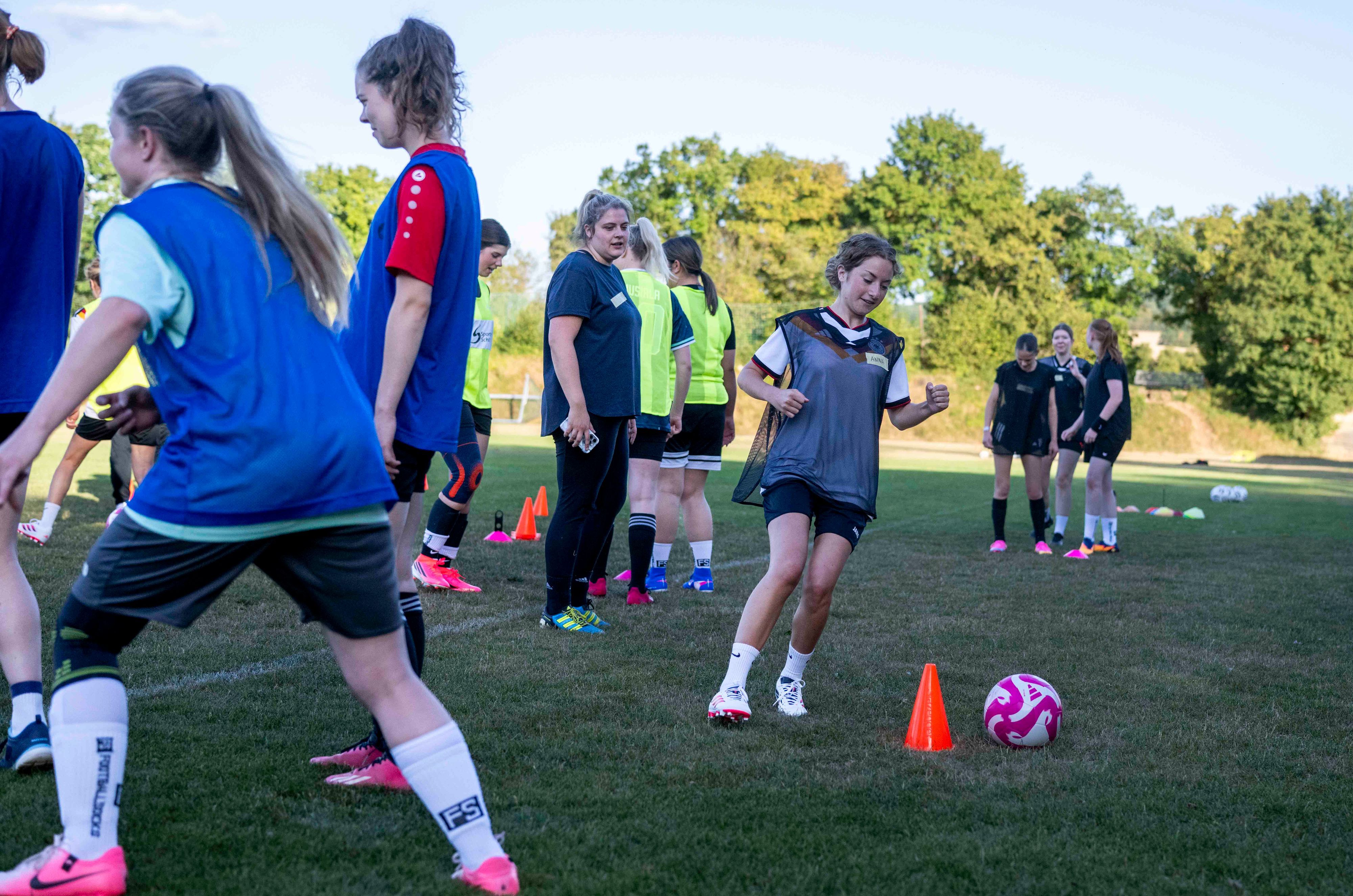 Eine Szene aus dem Training: Eine Spielerin dribbelt um einen Übungskegel herum, Mitspielerinnen schauen zu.
