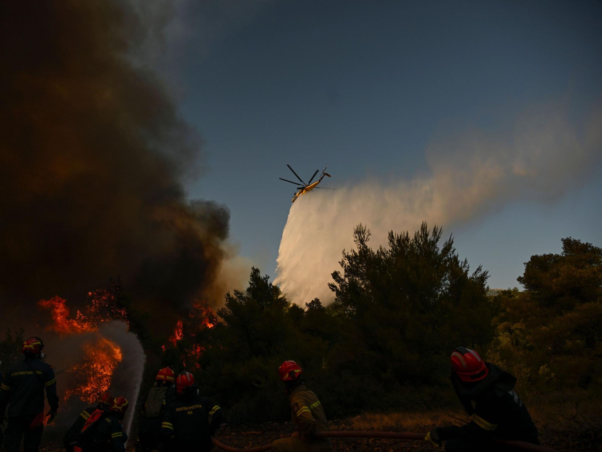Ein Löschhubschrauber wirft bei einem Waldbrand in der Nähe von Porto Germeno nordwestlich von Athen Löschmittel über einen rauchverhangenen Wald ab.