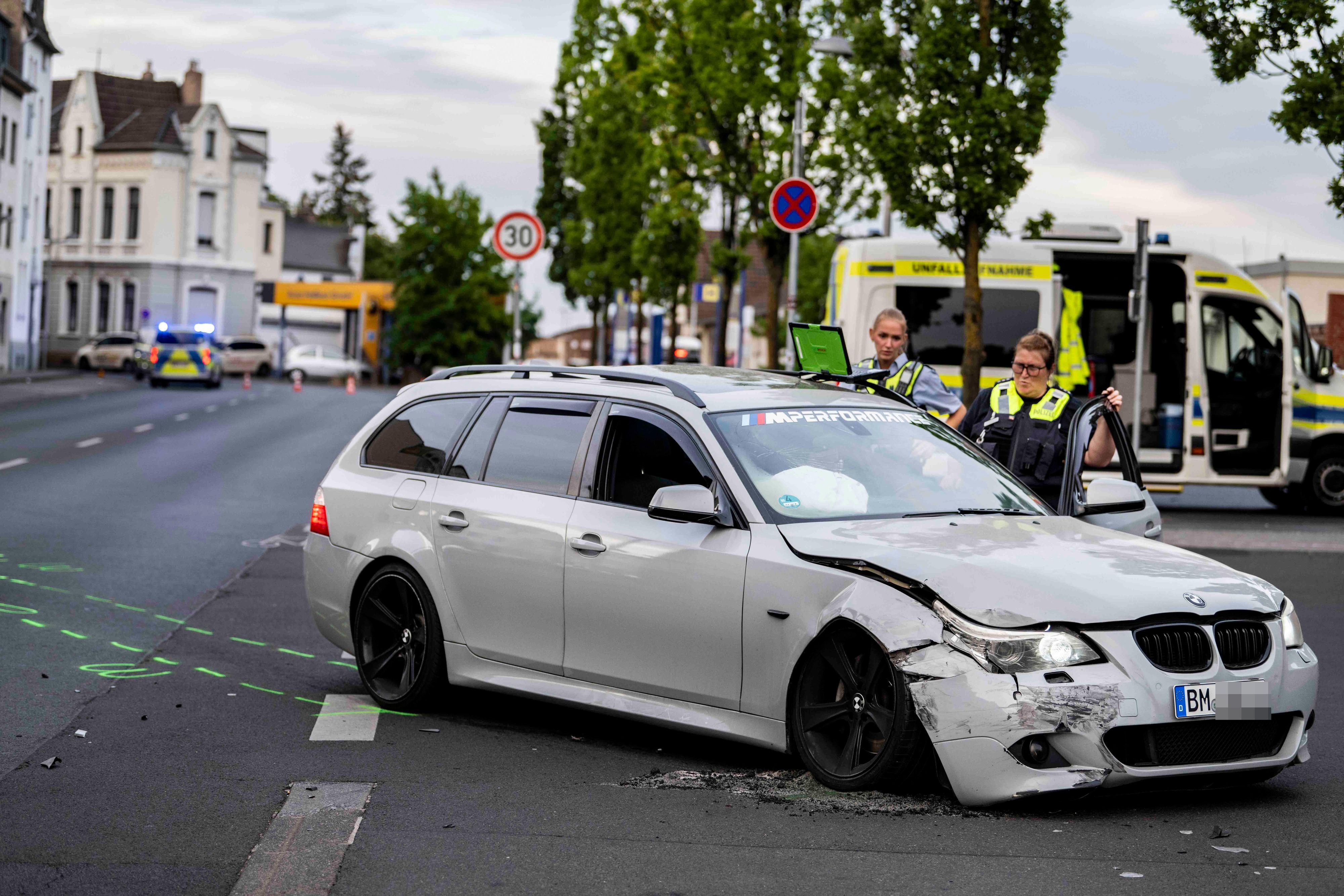 Das Foto zeigt im Vordergrund den beschädigten BMW Kombi und zwei weibliche Beamte vom Verkehrsunfallteam dahinter.