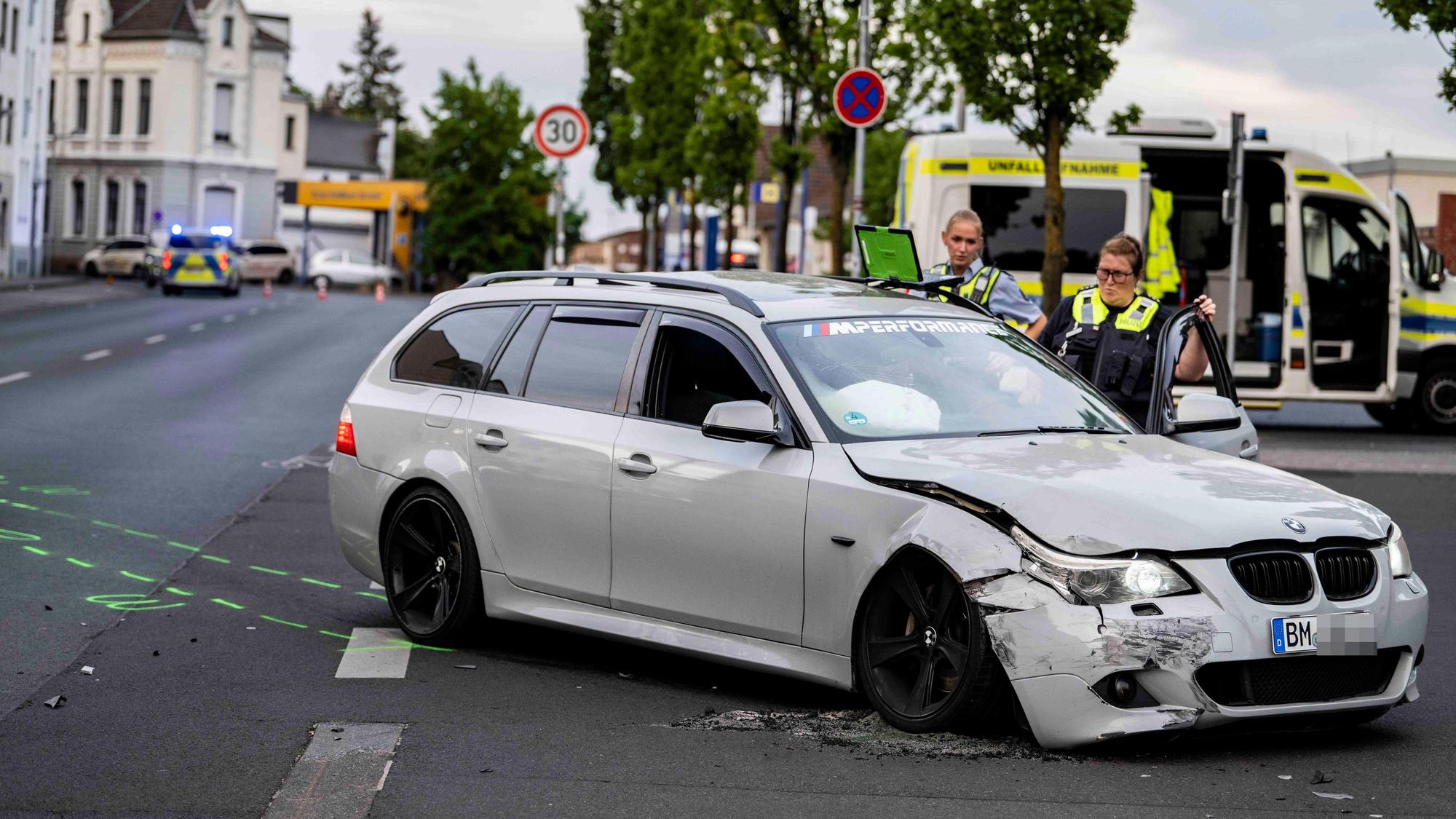 Das Foto zeigt im Vordergrund den beschädigten BMW Kombi und zwei weibliche Beamte vom Verkehrsunfallteam dahinter.
